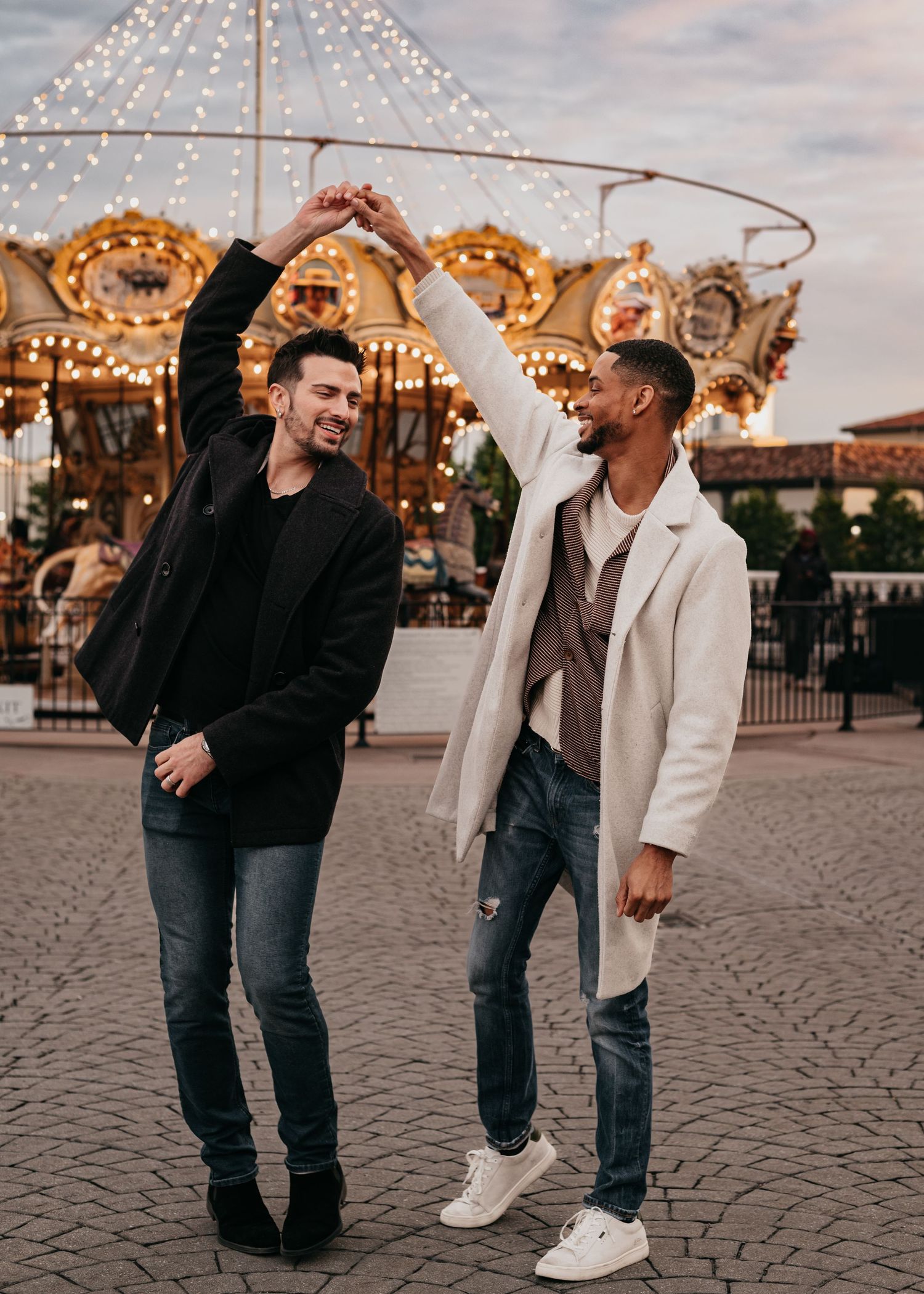 LGBTQ+ couple celebrating with a dance together during engagement proposal beside carousel lights at Bridge Street