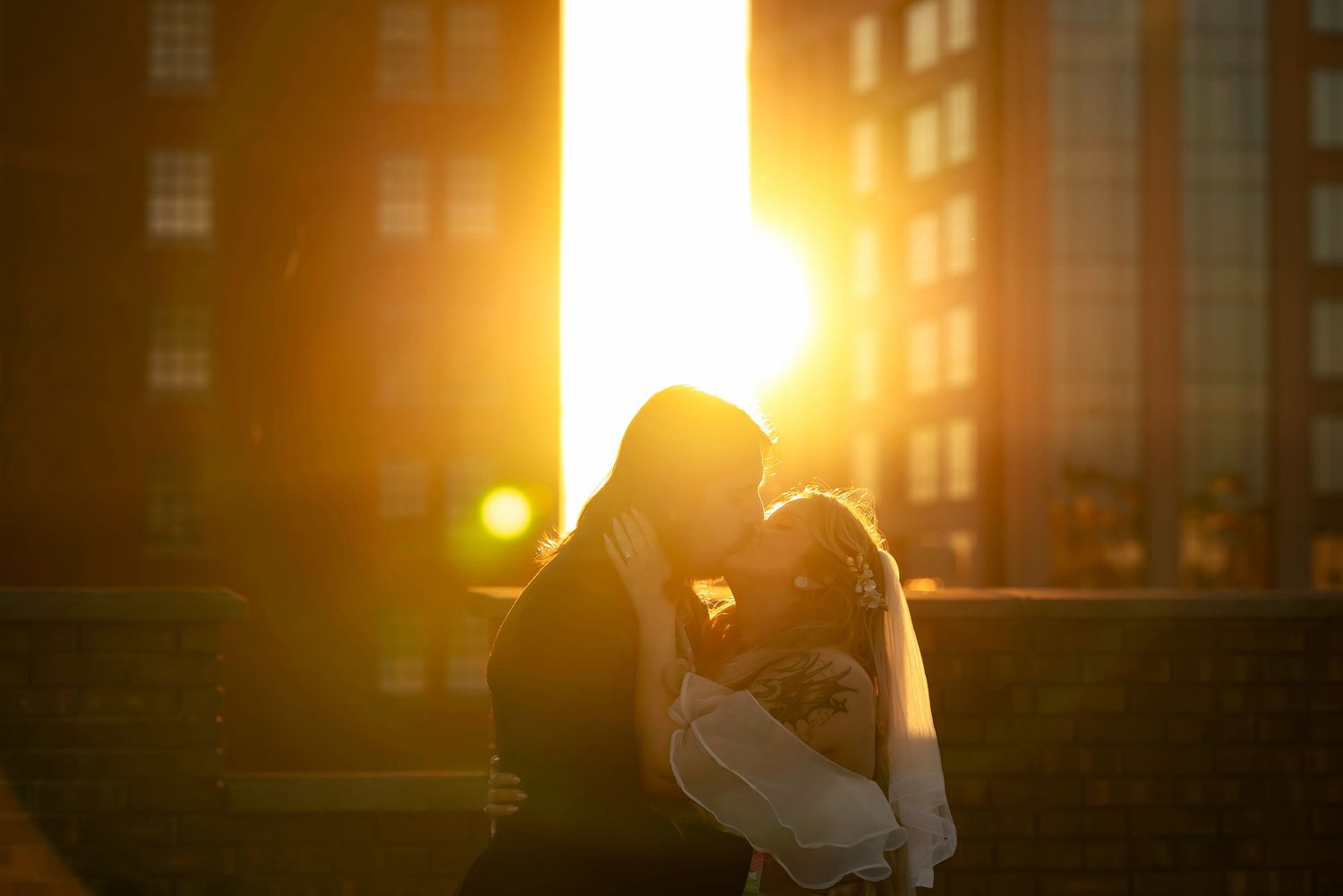 Bride and groom sharing glowing, silhouetted kiss on downtown rooftop at sunset, captured by Catch Your Fire Photography in Huntsville, AL.
