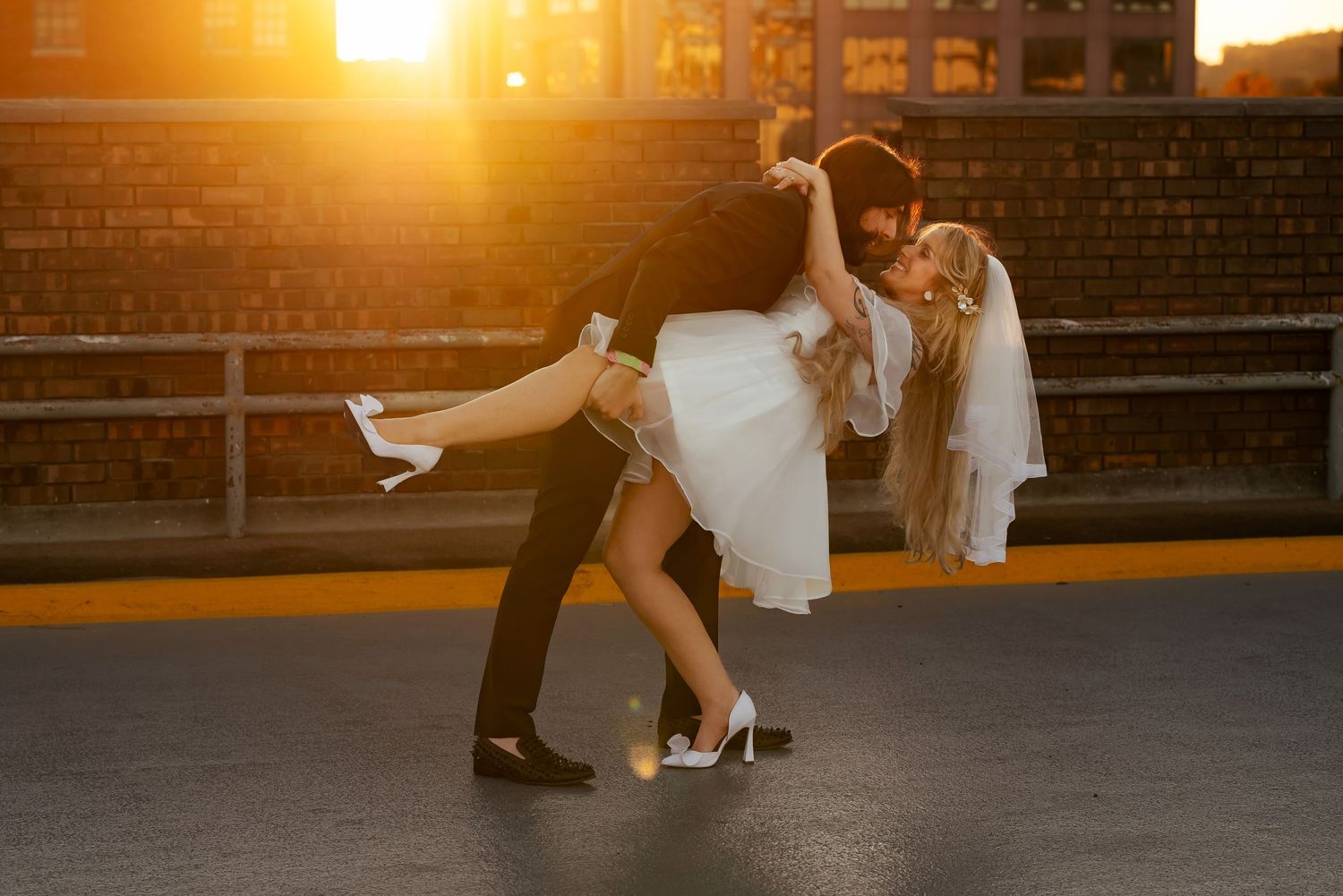 Bride and groom sharing playful dip on rooftop at sunset, smiling and leaning in for kiss, captured by Catch Your Fire in Huntsville, AL.