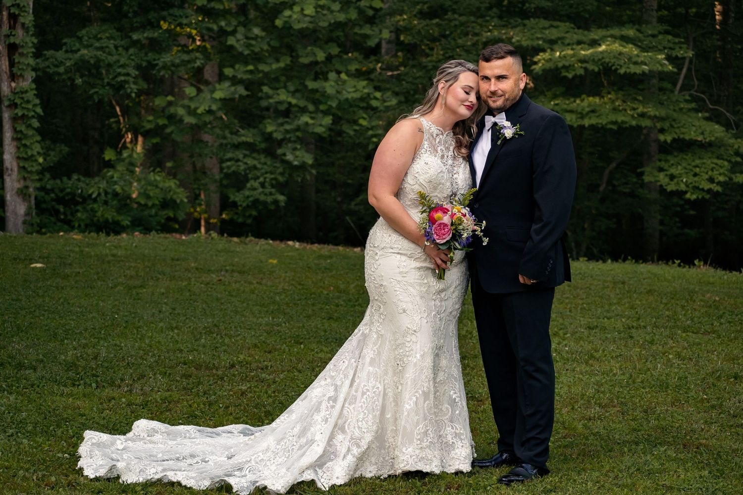 Happy bride leaning on groom’s shoulder with closed eyes, lush green trees behind them, at Ivy Oaks venue near Huntsville, in New Market, AL