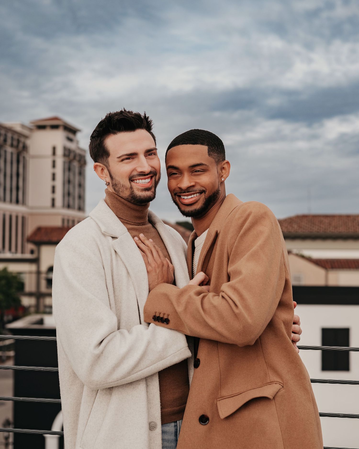 Same-sex couple cuddling and smiling on parking garage rooftop overlooking Bridge Street