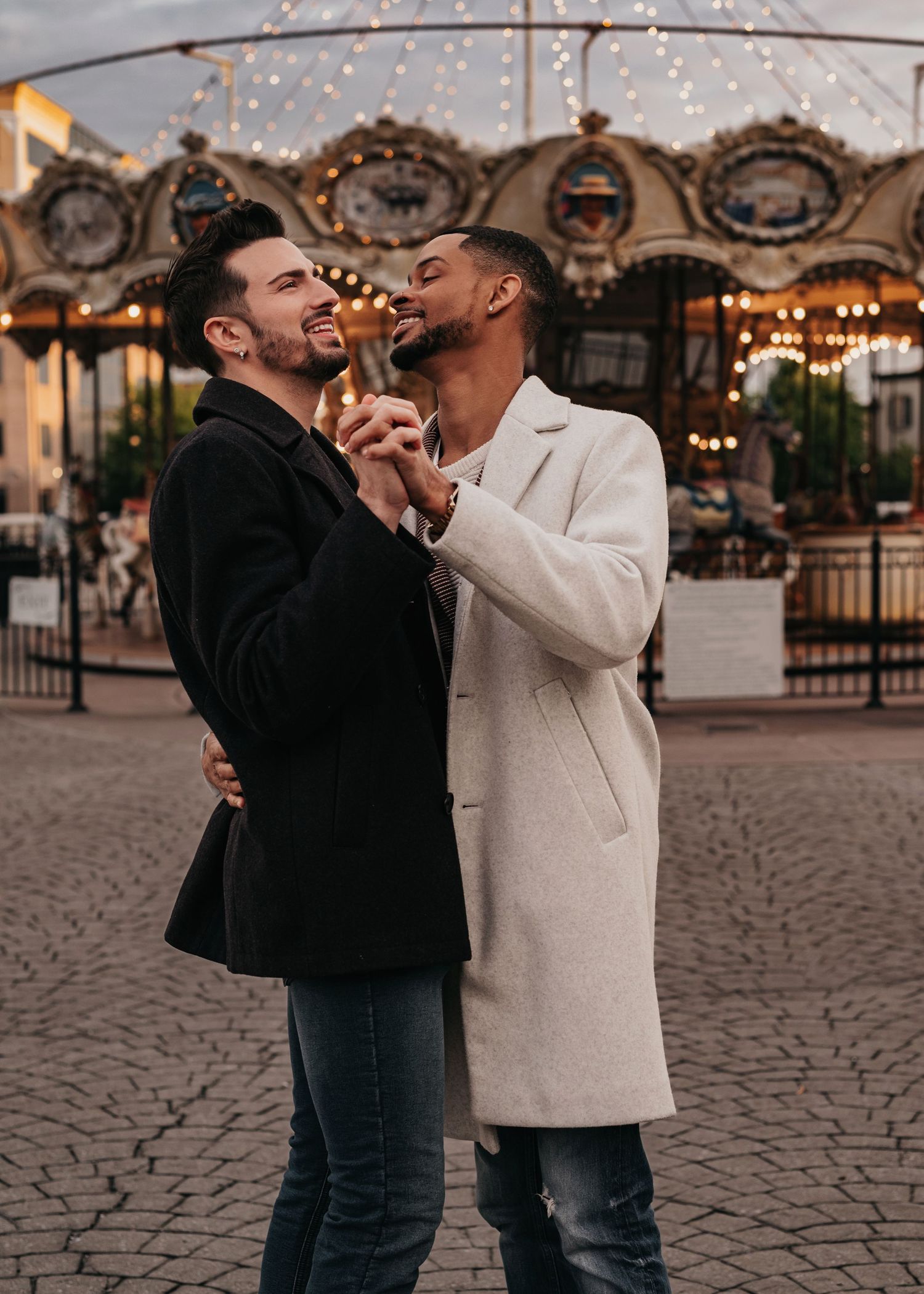 LGBTQ+ couple embracing after engagement proposal beside carousel lights at Bridge Street