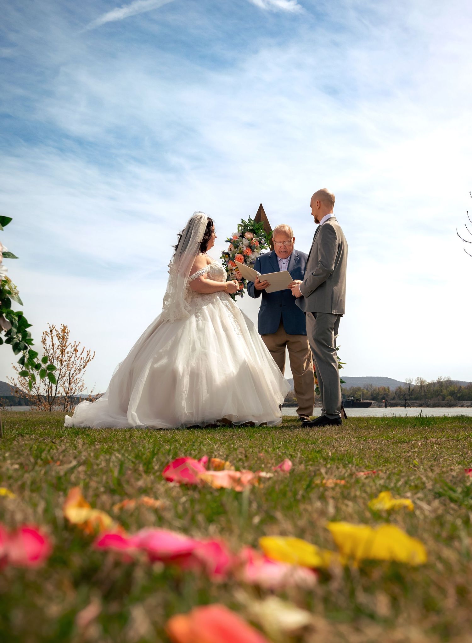 Bride and groom saying vows on flower-dusted riverside walkway at bright spring afternoon wedding, in Huntsville, Alabama