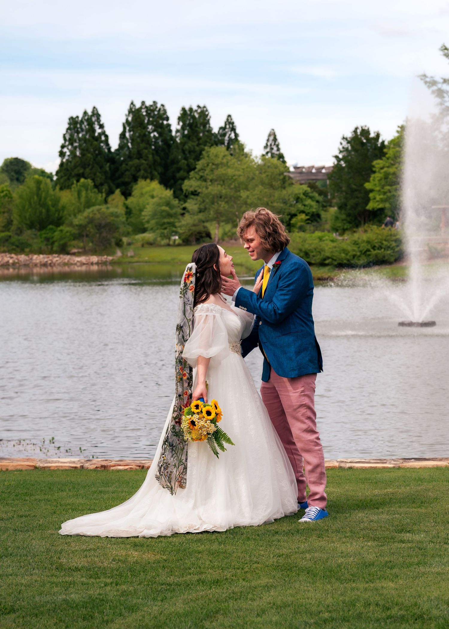 Romantic couple by fountain lake at Huntsville Botanical Garden with groom holding bride’s chin before a kiss