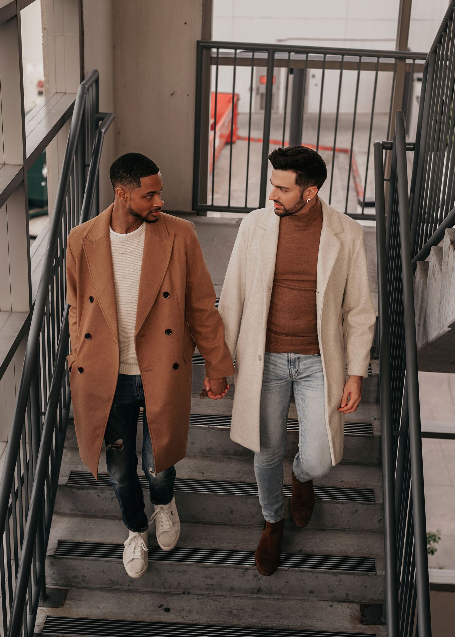 interracial same sex couple holding hands, walking down stairs, looking at each other
