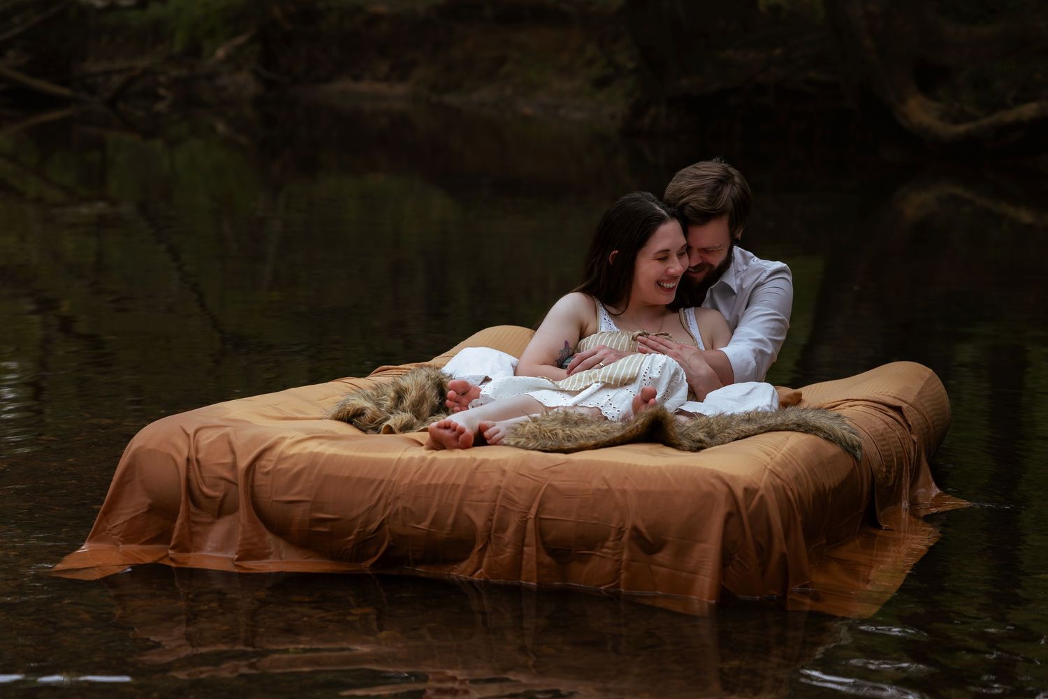 Whimsical outdoor moment: couple snuggling on floating bed in creek, photographed by Catch Your Fire Photography in Huntsville, AL.