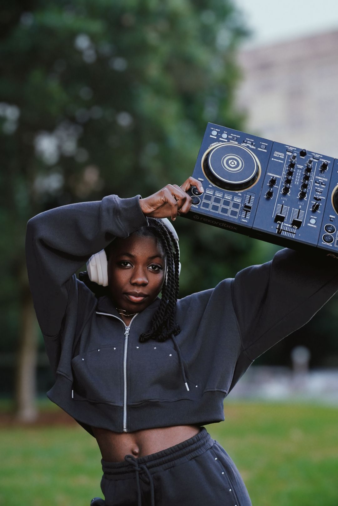 Female DJ carrying Pioneer DJ controller on shoulder outdoors.