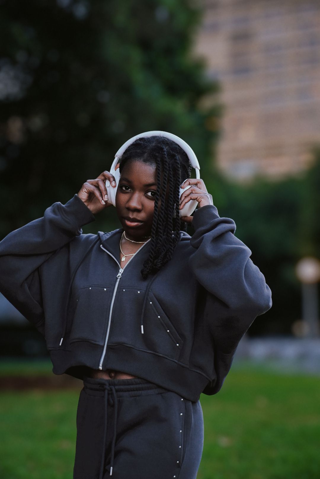Woman in dark tracksuit putting on white headphones in park.