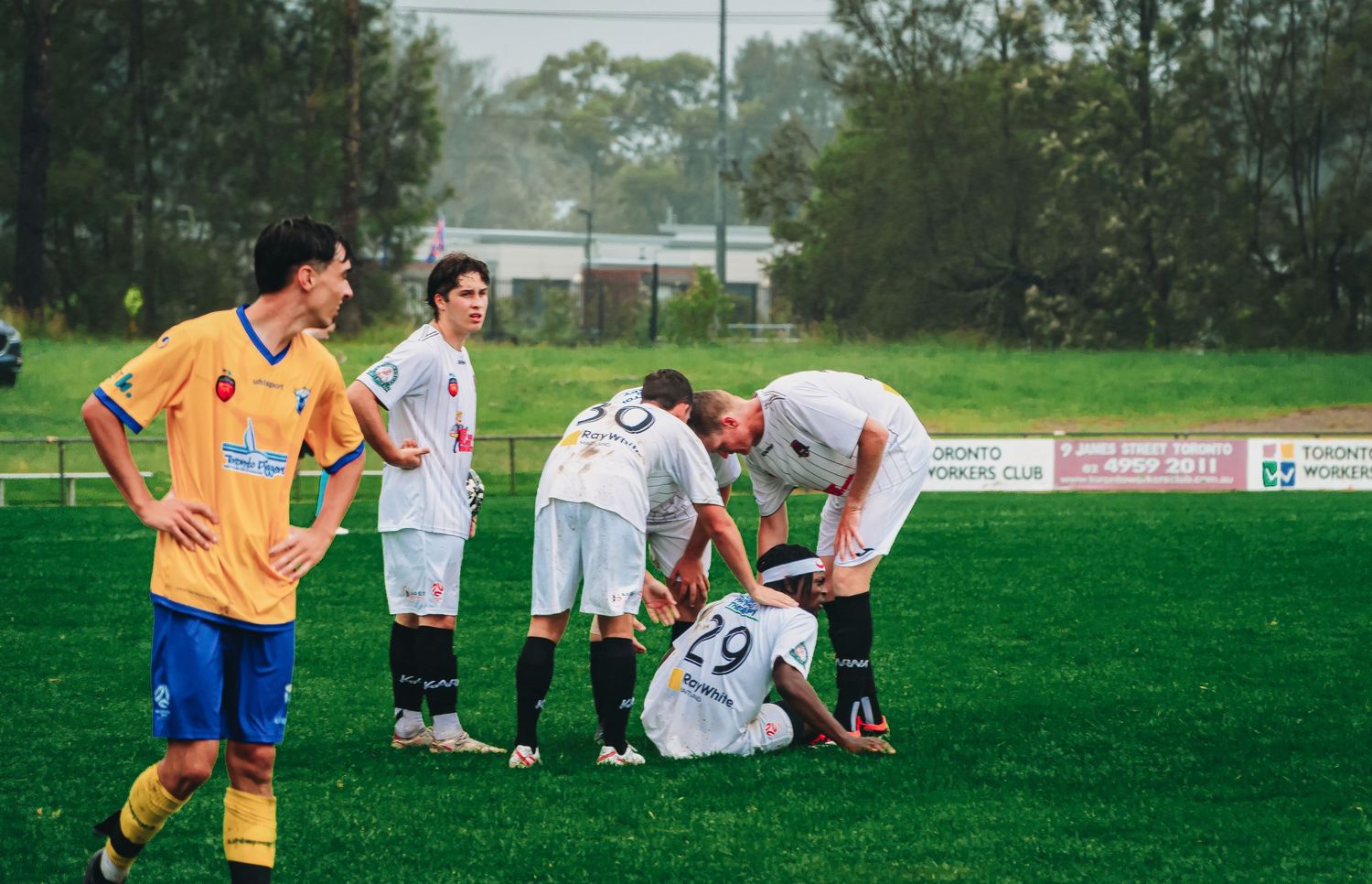 Soccer players gather around an injured teammate on the grass field during a match, showing concern and sportsmanship.