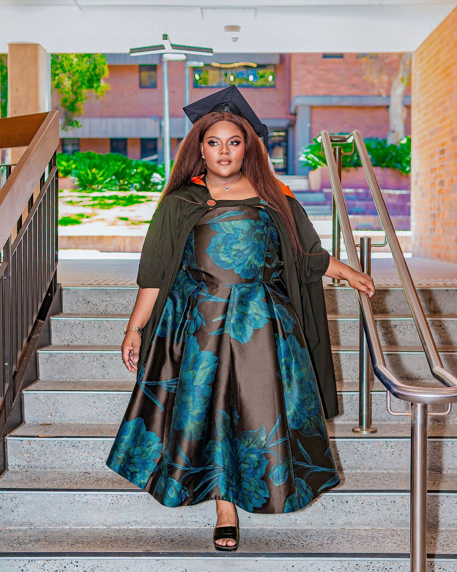 Graduate in floral gown and cap descends stairs outdoors.