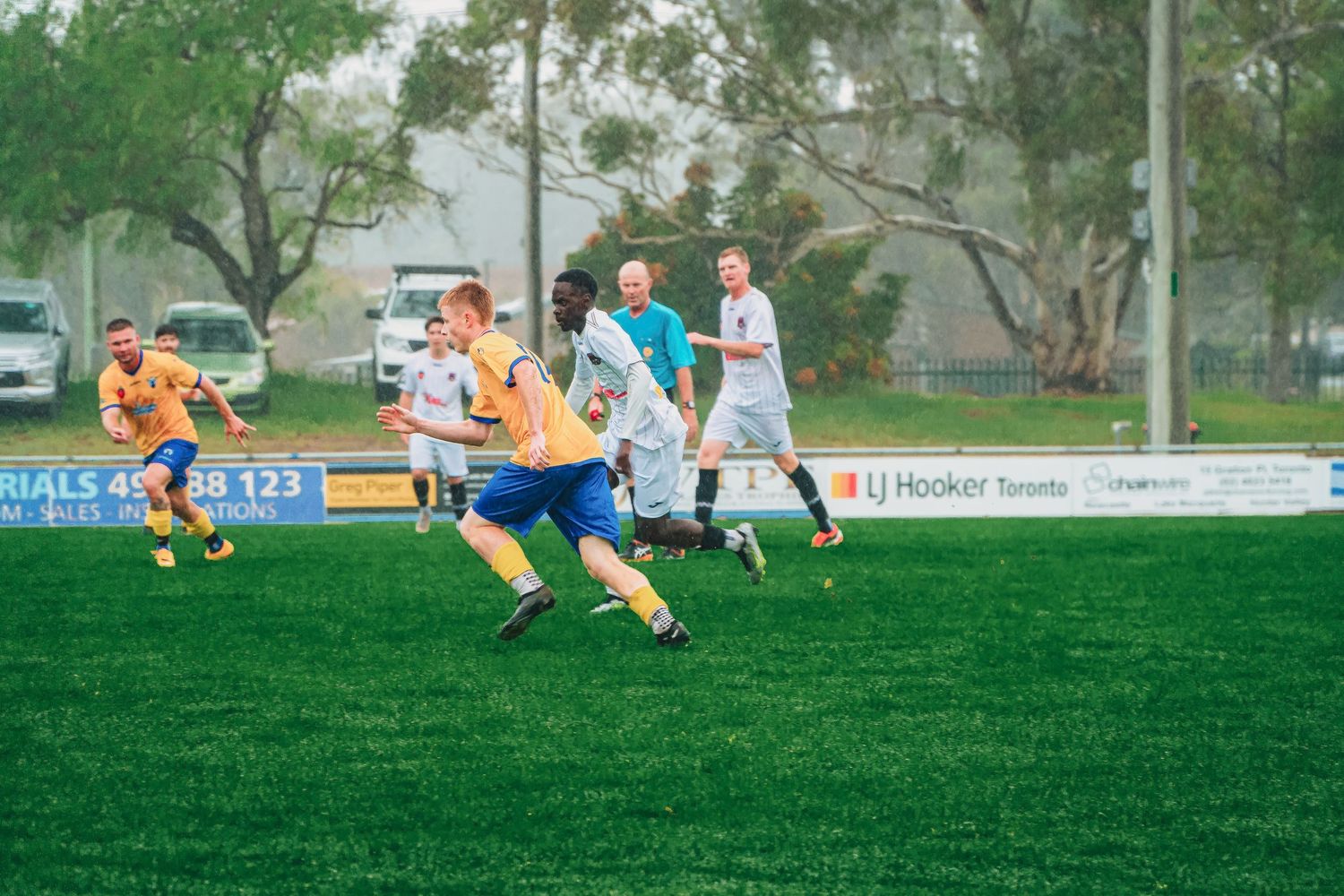 Soccer players in orange and white jerseys compete during an outdoor match on a green grass field.