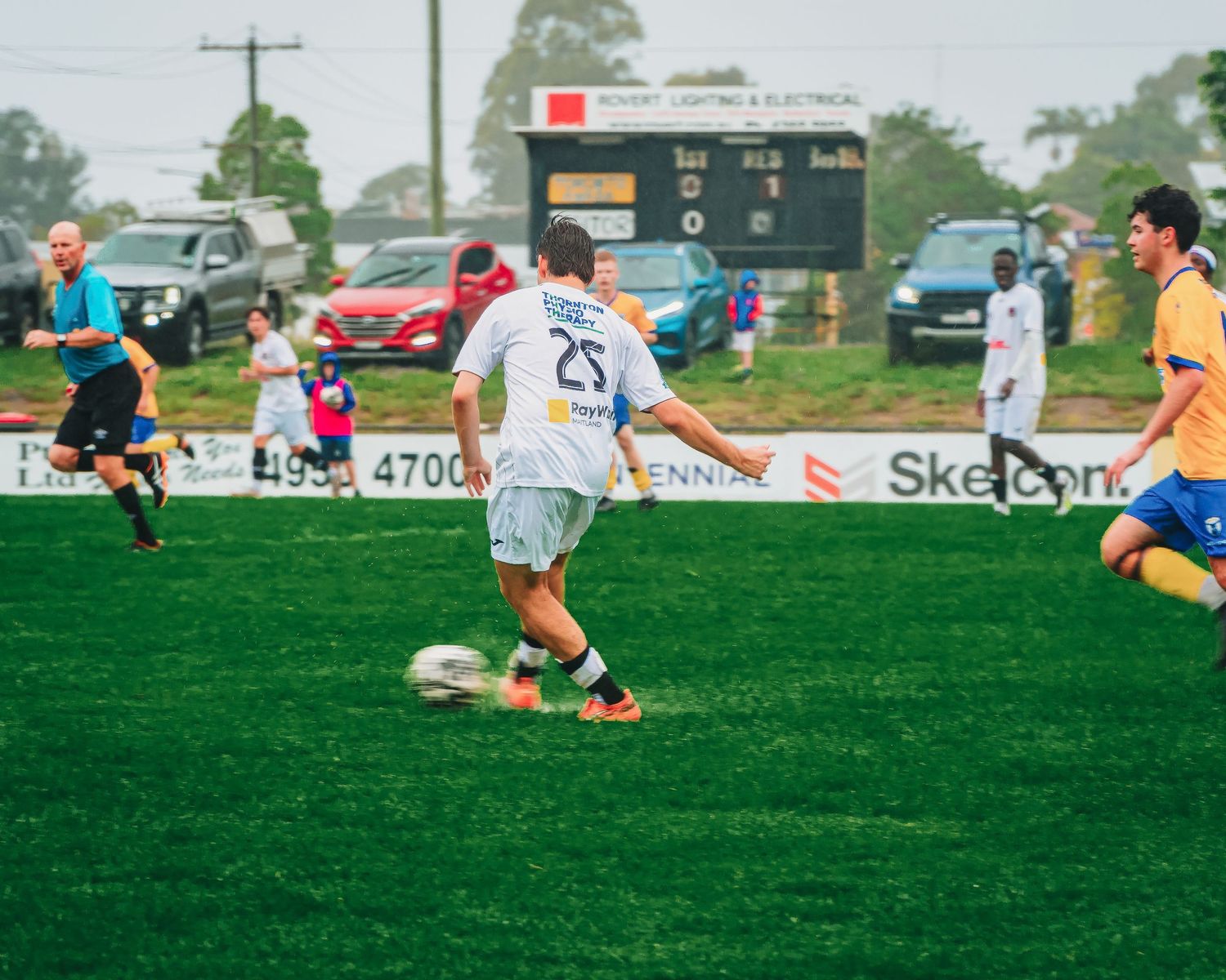 Soccer players compete on a green field during a rainy match, with player 25 controlling the ball.