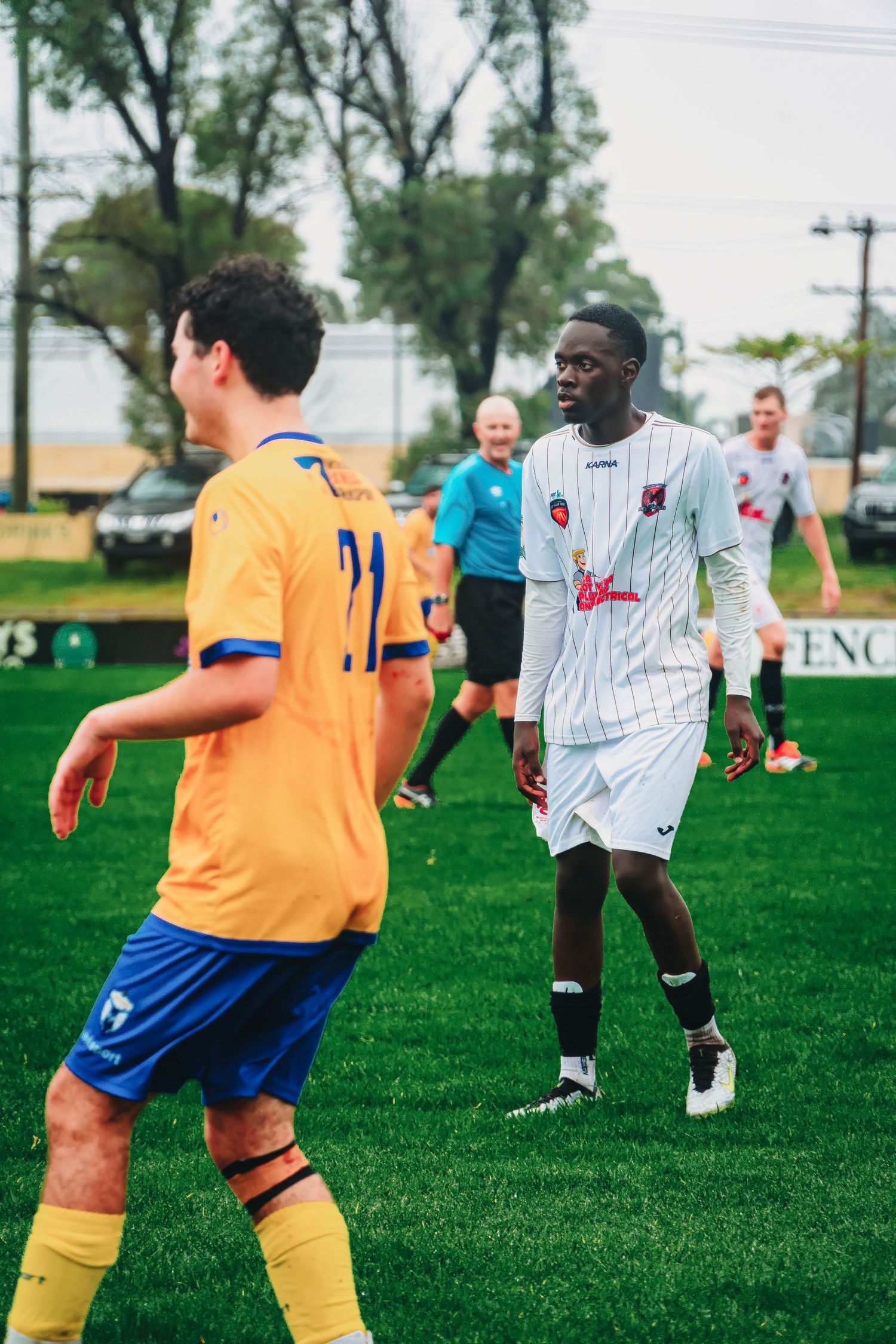 Soccer players in yellow and white jerseys compete on a green grass field during an outdoor match.