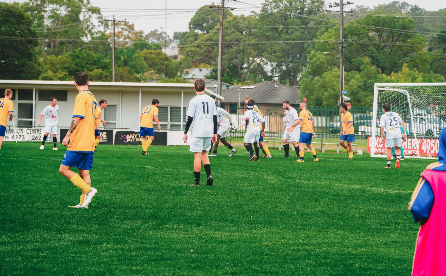 Soccer players in yellow and white uniforms compete on a green field during an outdoor match.