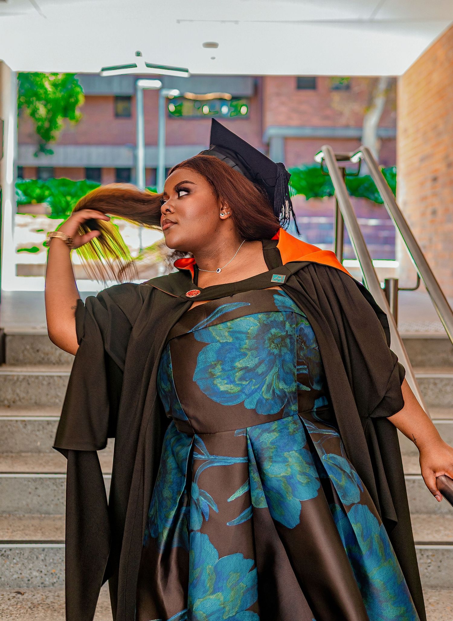 Graduate in black gown and cap posing on steps, flipping hair confidently.