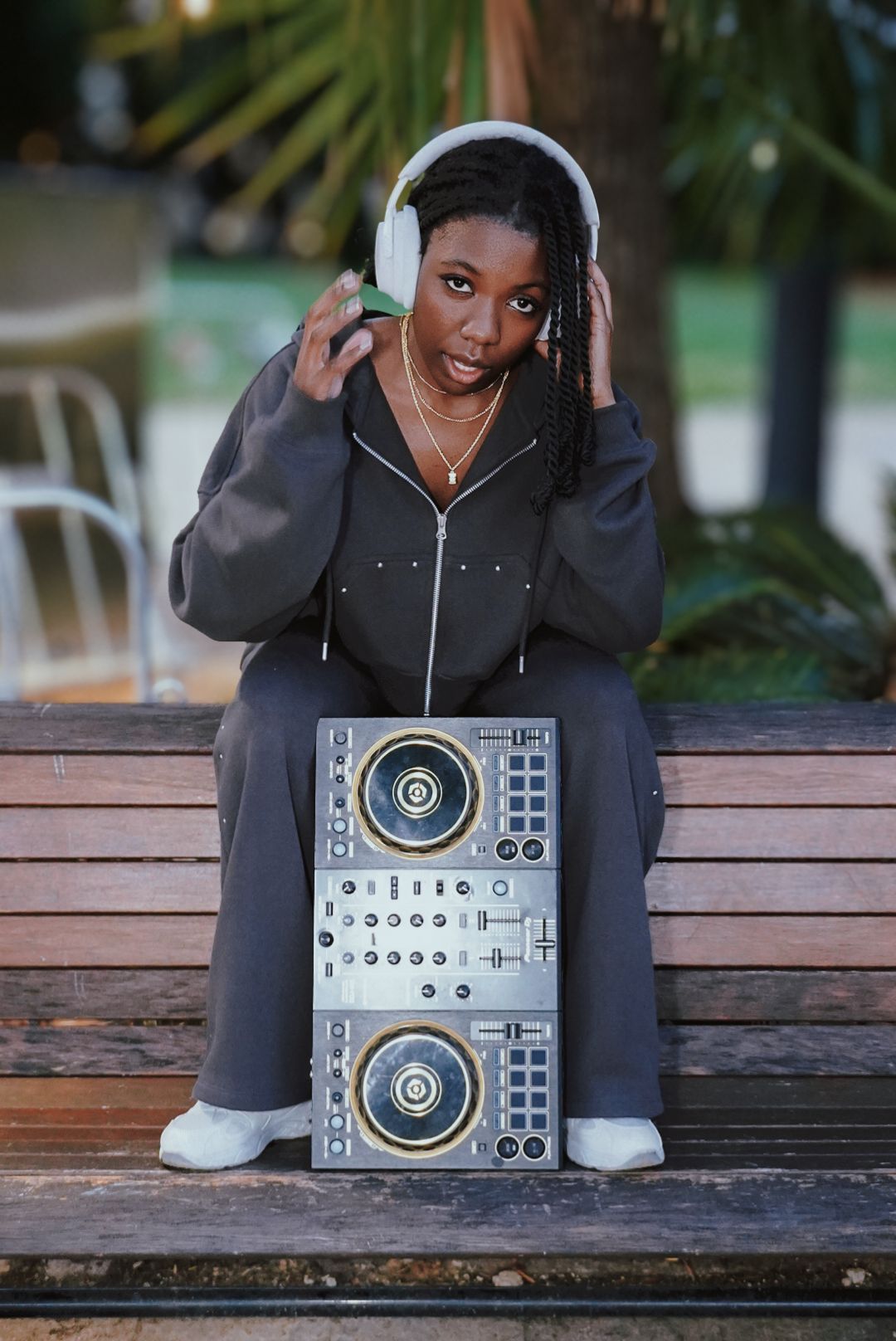 Woman sitting on bench with DJ controller wearing white headphones.