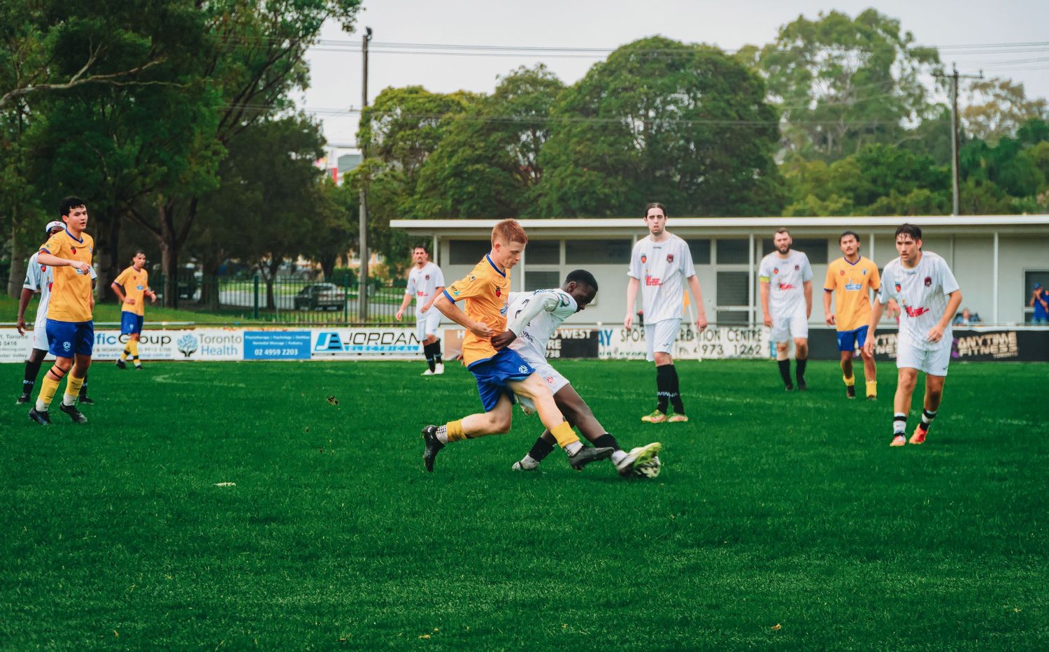 Two soccer players battle for the ball on a green pitch during a competitive outdoor football match.