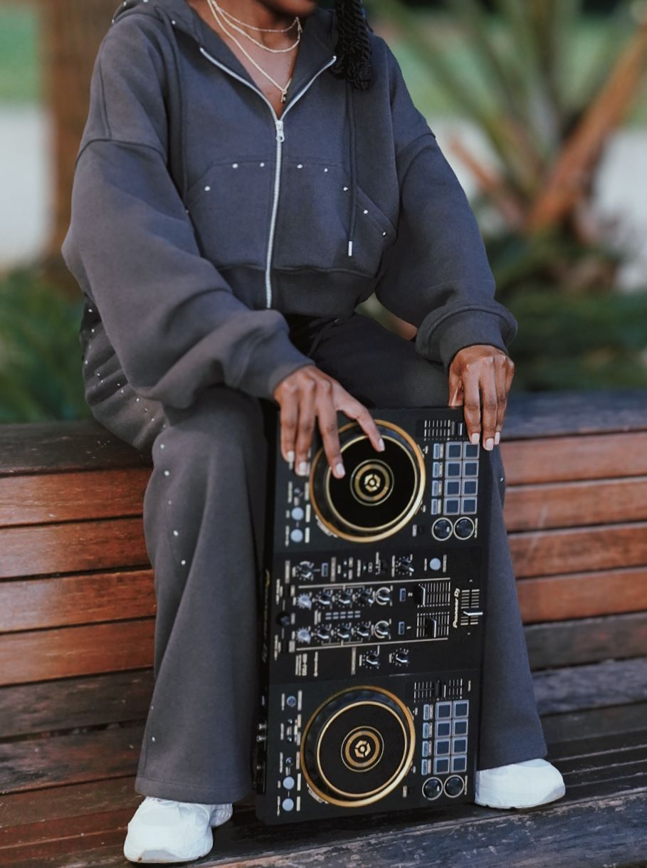 Close-up of woman in gray zip hoodie operating a DJ controller on a bench outdoors.