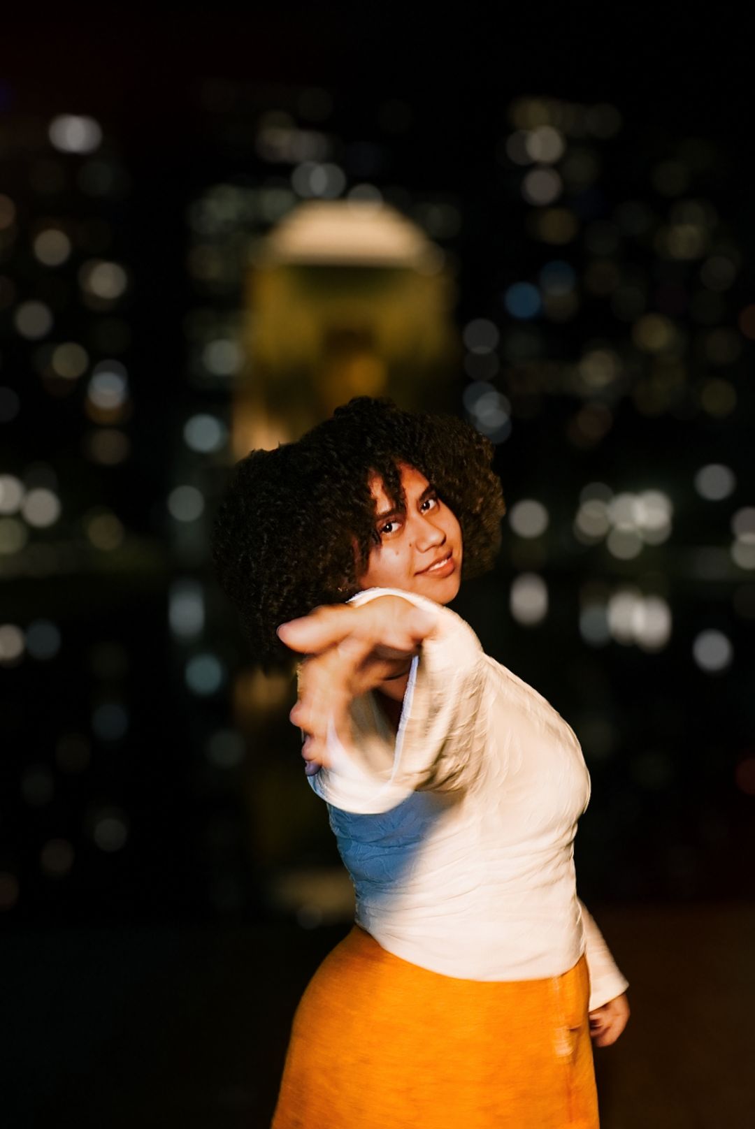 Woman in white top and orange skirt reaching toward camera during a creative nighttime photo session.