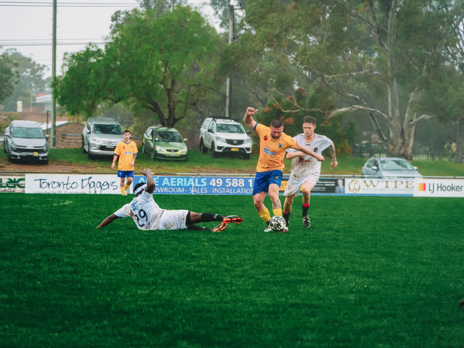 Soccer players clash on a green field as one player slides in a tackle during an outdoor match.