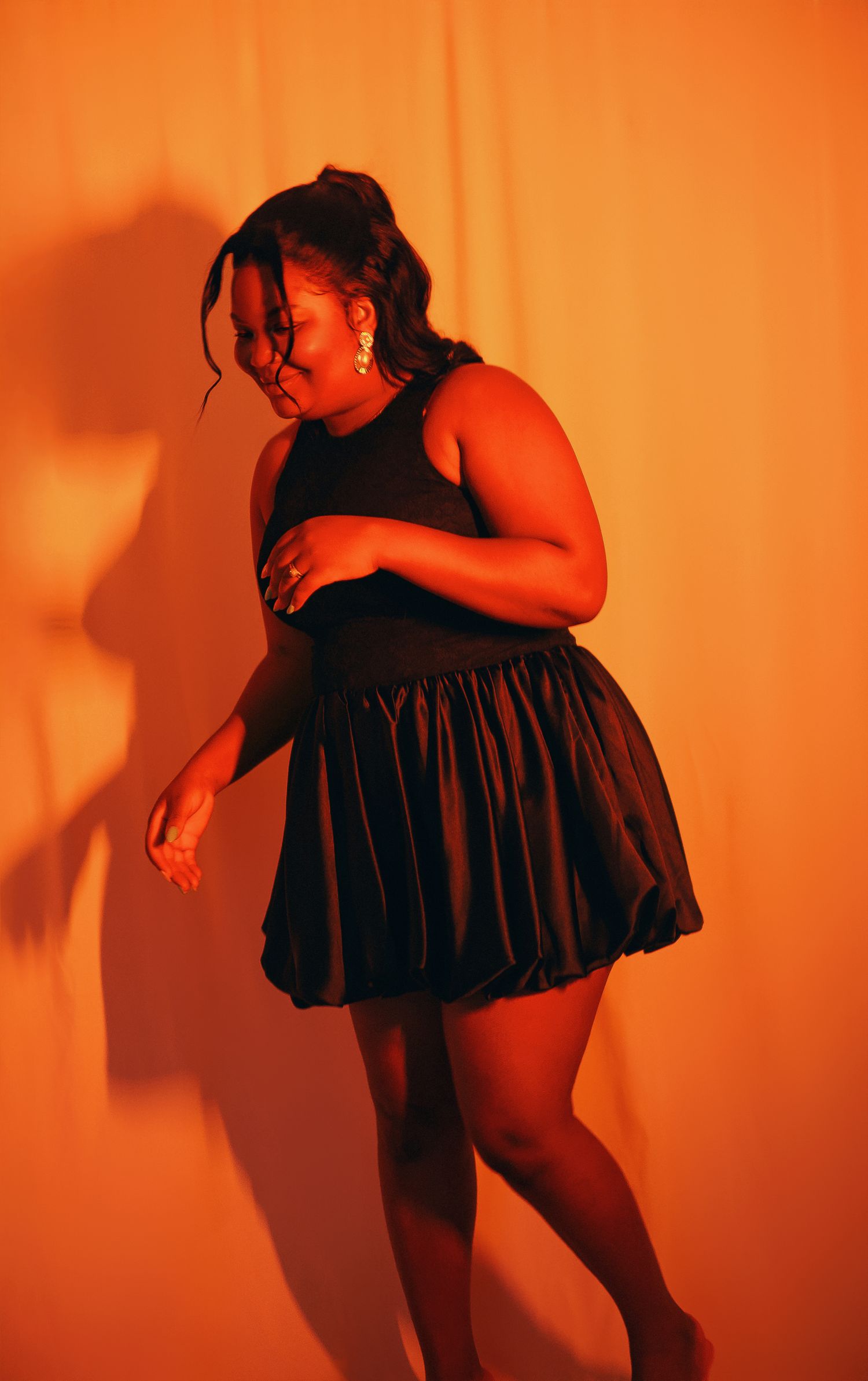 Woman in black bubble mini dress dancing against orange backdrop.