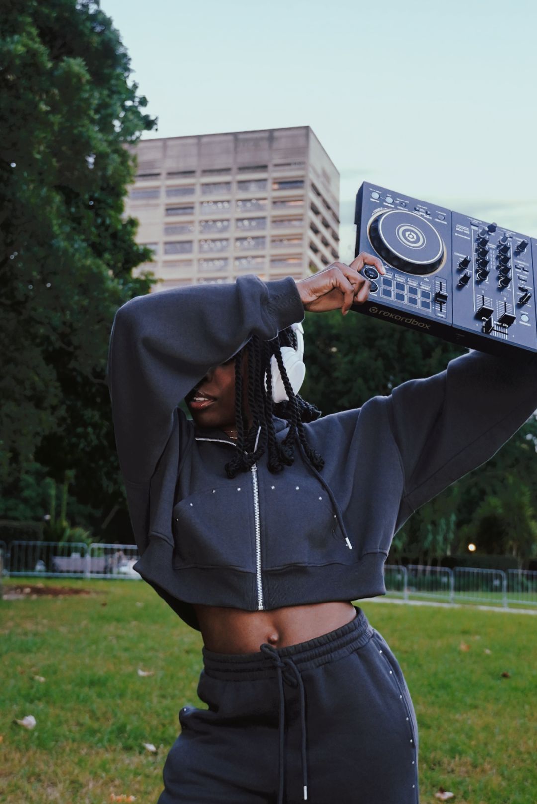 Woman balancing DJ controller overhead in urban park setting.