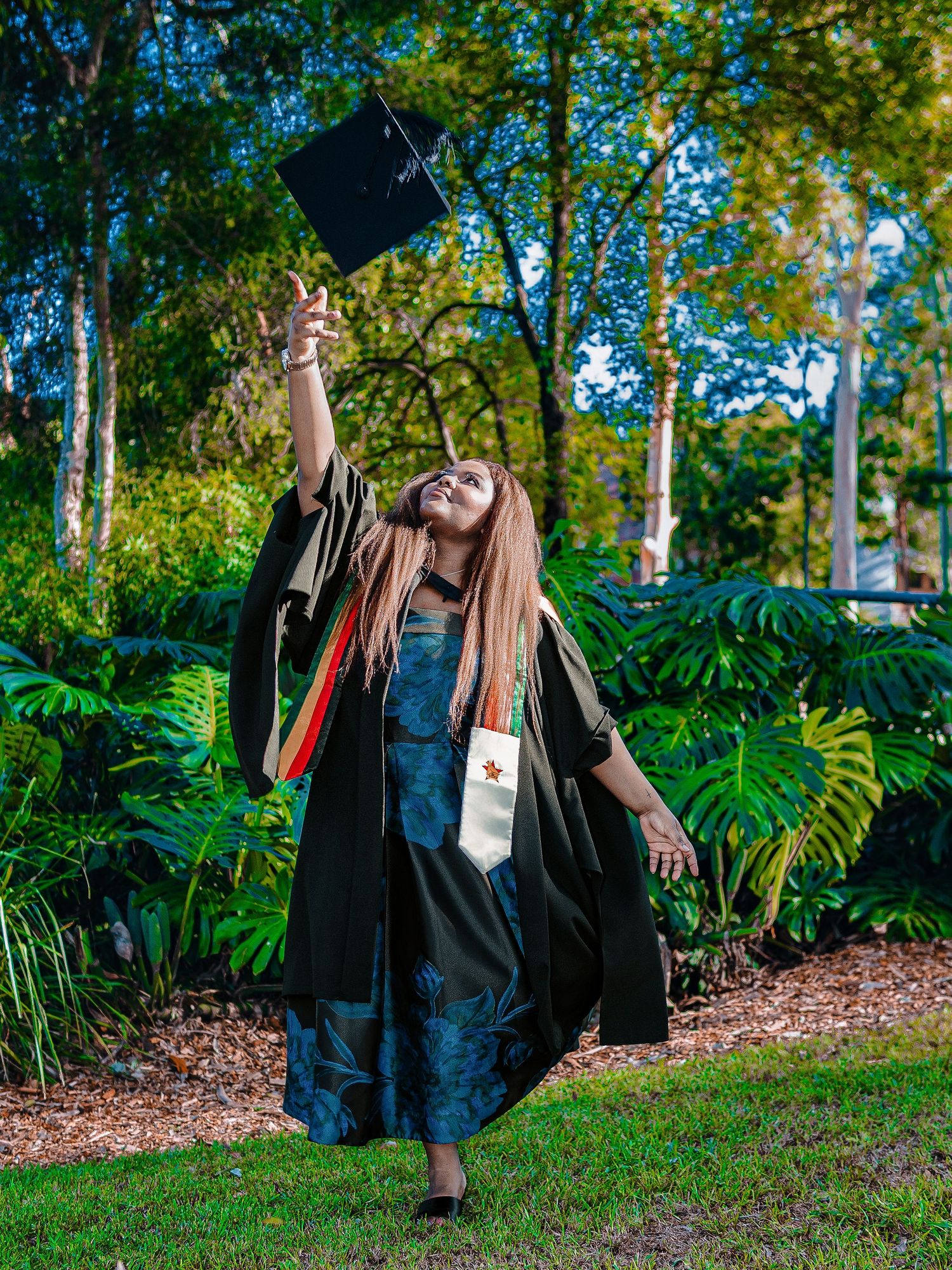 Joyful graduate tossing mortarboard cap in lush green garden during outdoor graduation celebration.