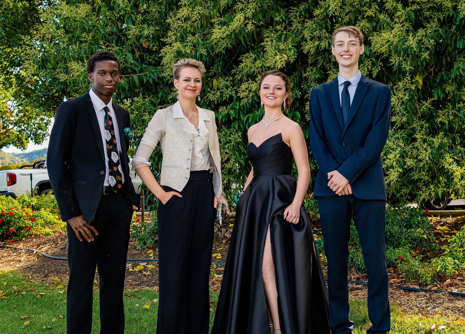 Four elegantly dressed young adults posing together in formal attire at an outdoor garden event.