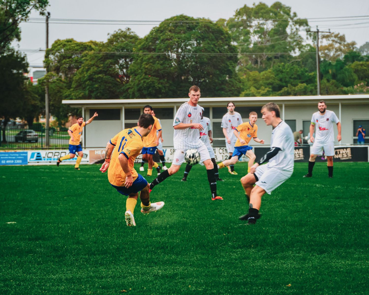 Soccer players in yellow and white uniforms compete for the ball on a green field during an outdoor match.