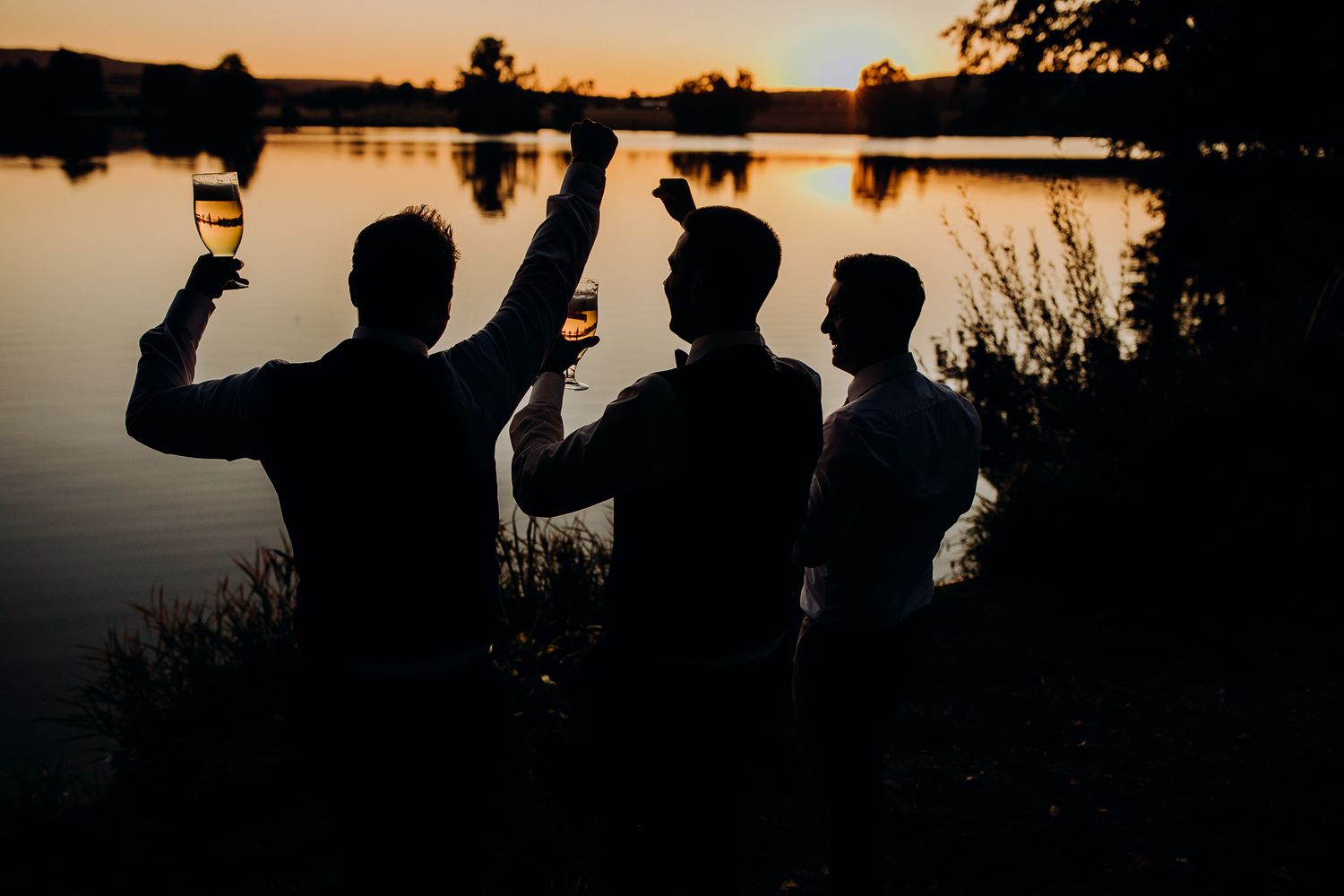 Silhouette von Gästen am See bei Sonnenuntergang während einer Hochzeitsfeier Bräutigam und Freunde