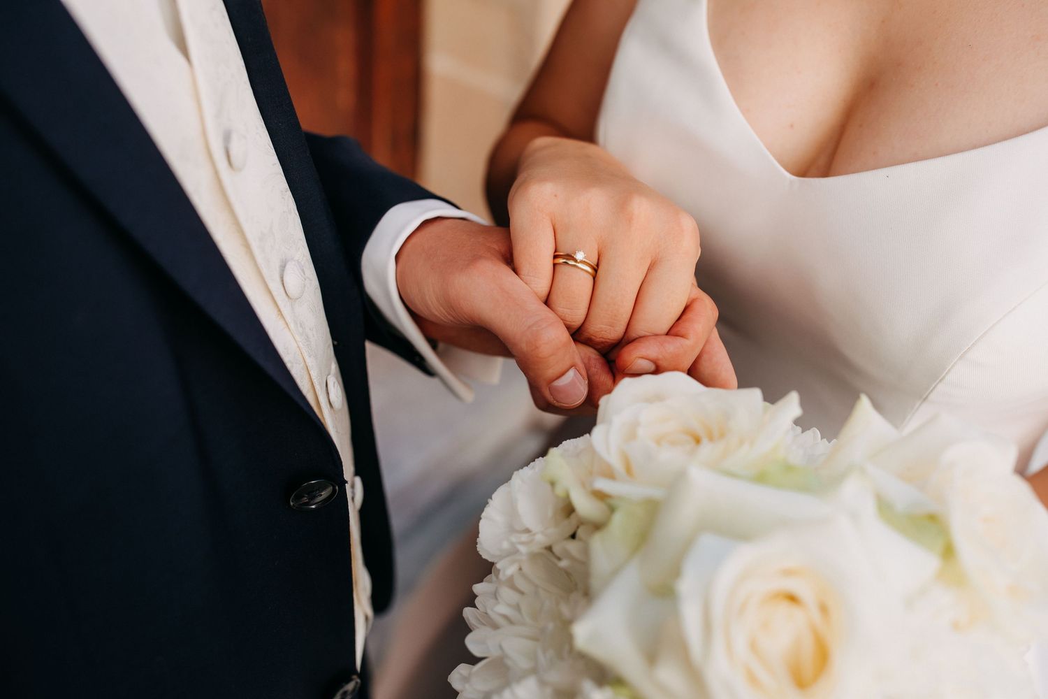 Detailaufnahme von Händen mit Eheringen und Brautstrauß während der Hochzeit