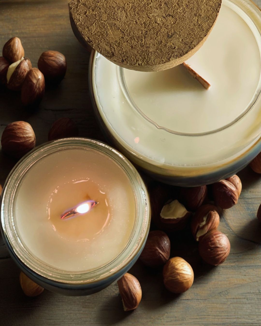 Scented candles with hazelnuts scattered on dark wooden surface creating cozy atmosphere.