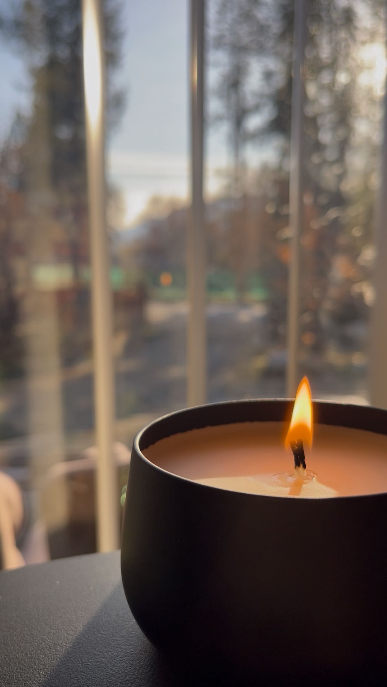 Lit candle in a dark bowl against a blurred outdoor background creates a cozy ambiance.