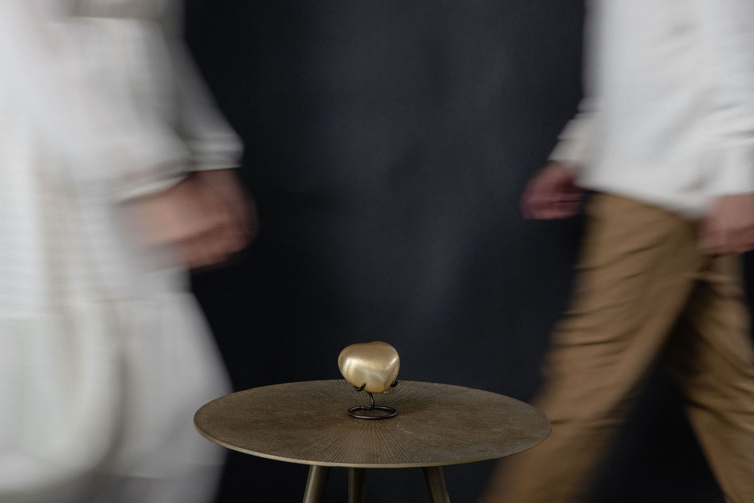 Blurry two people passing by eachother behind a heart shaped urn