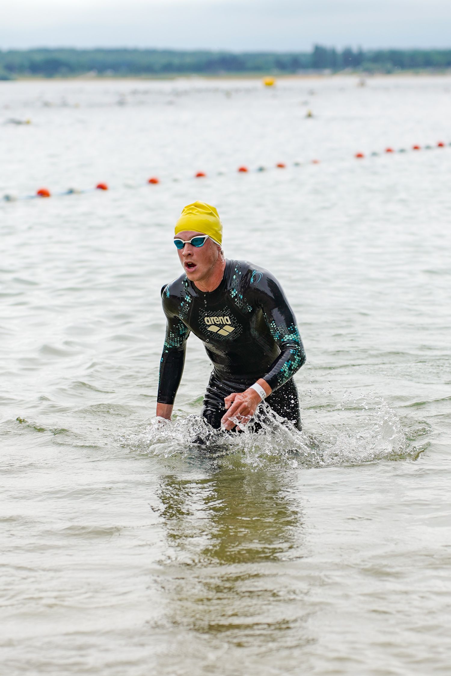 Triathlete emerges from water wearing wetsuit and yellow swim cap during competition.