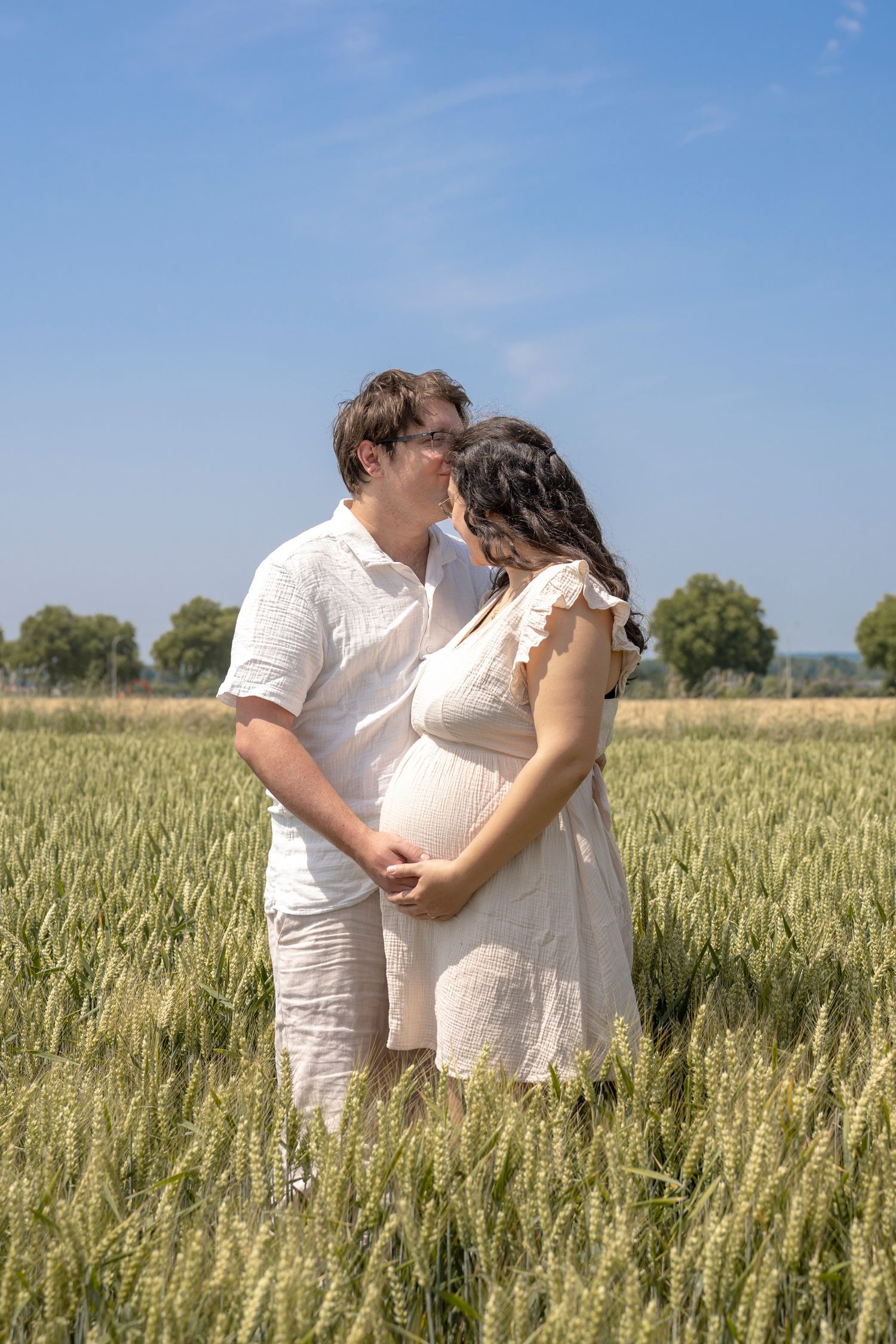 Couple in white clothing embraces romantically among tall wheat stalks on sunny day.