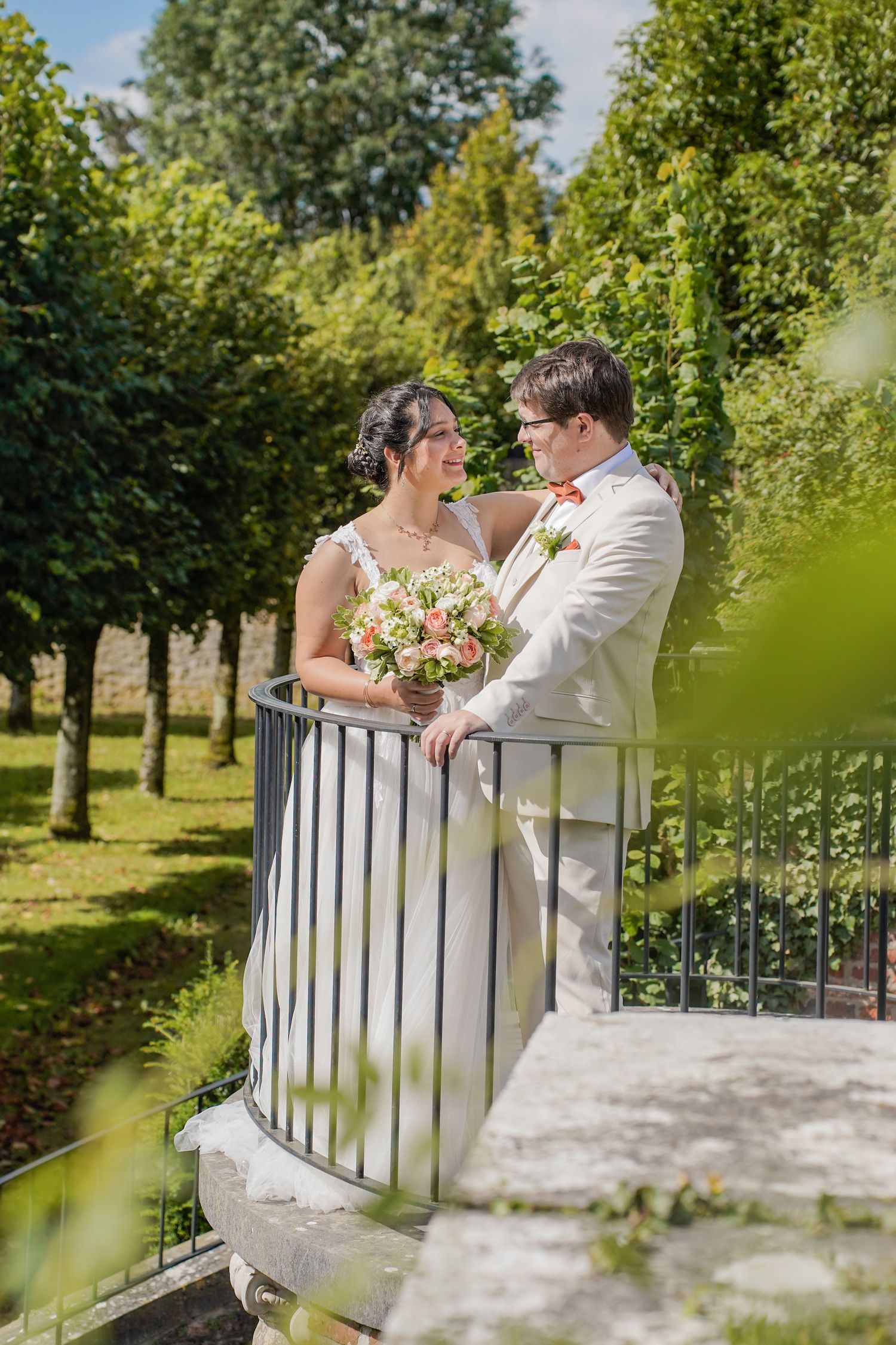 Wedding couple shares intimate moments on a white bridge surrounded by greenery.