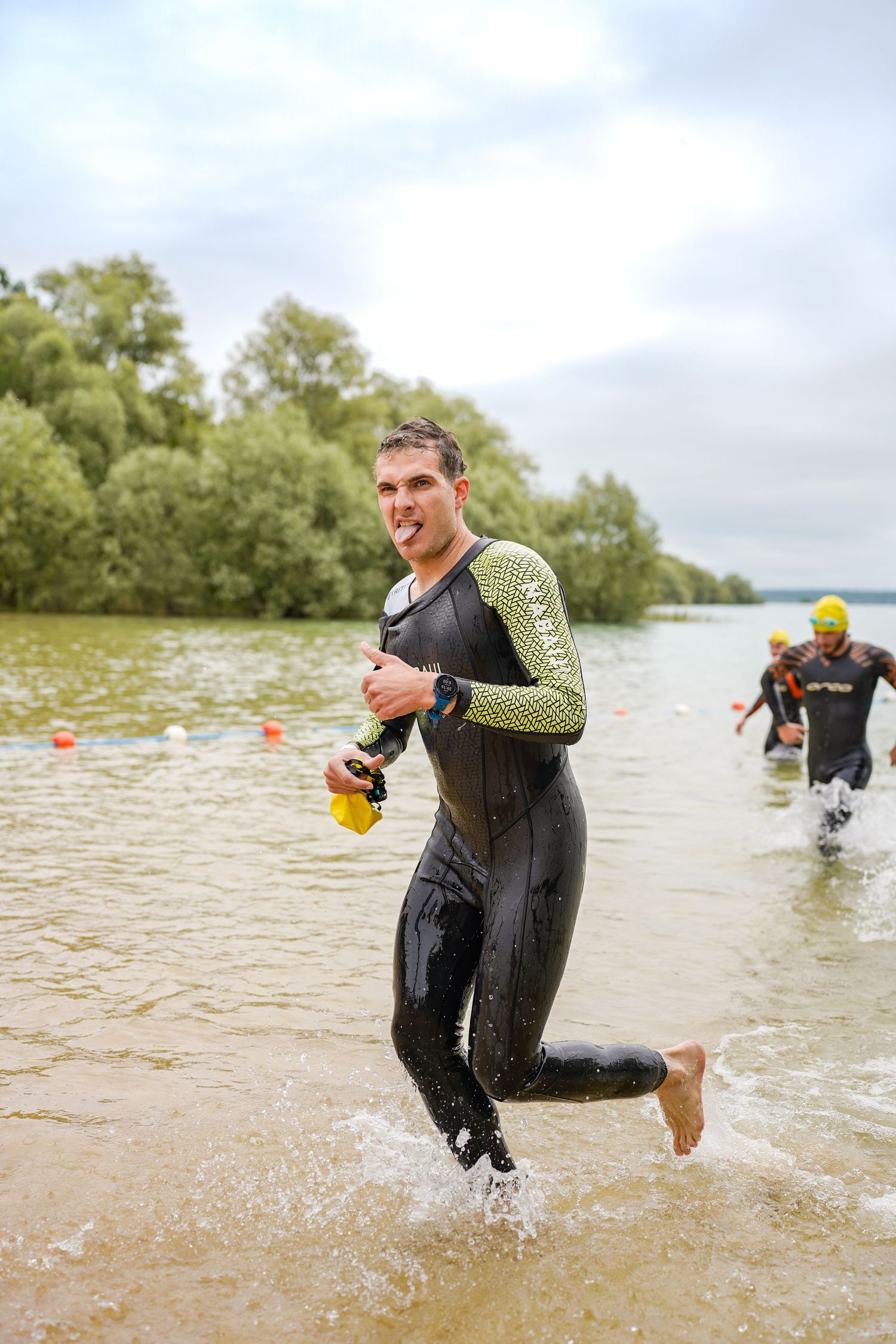 Athletes in wetsuits splash through shallow water during triathlon race.