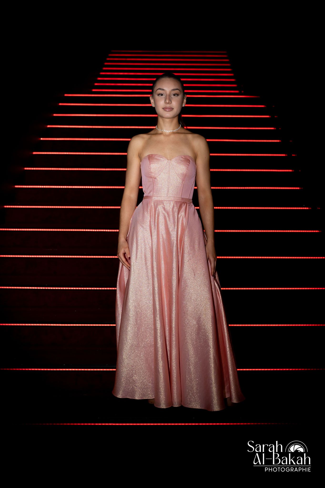 Fashion portrait on red-lit stairs wearing a pink satin gown.