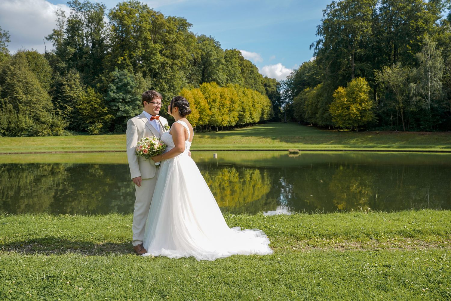 Wedding photography session in a scenic park with a lake and trees in the background.