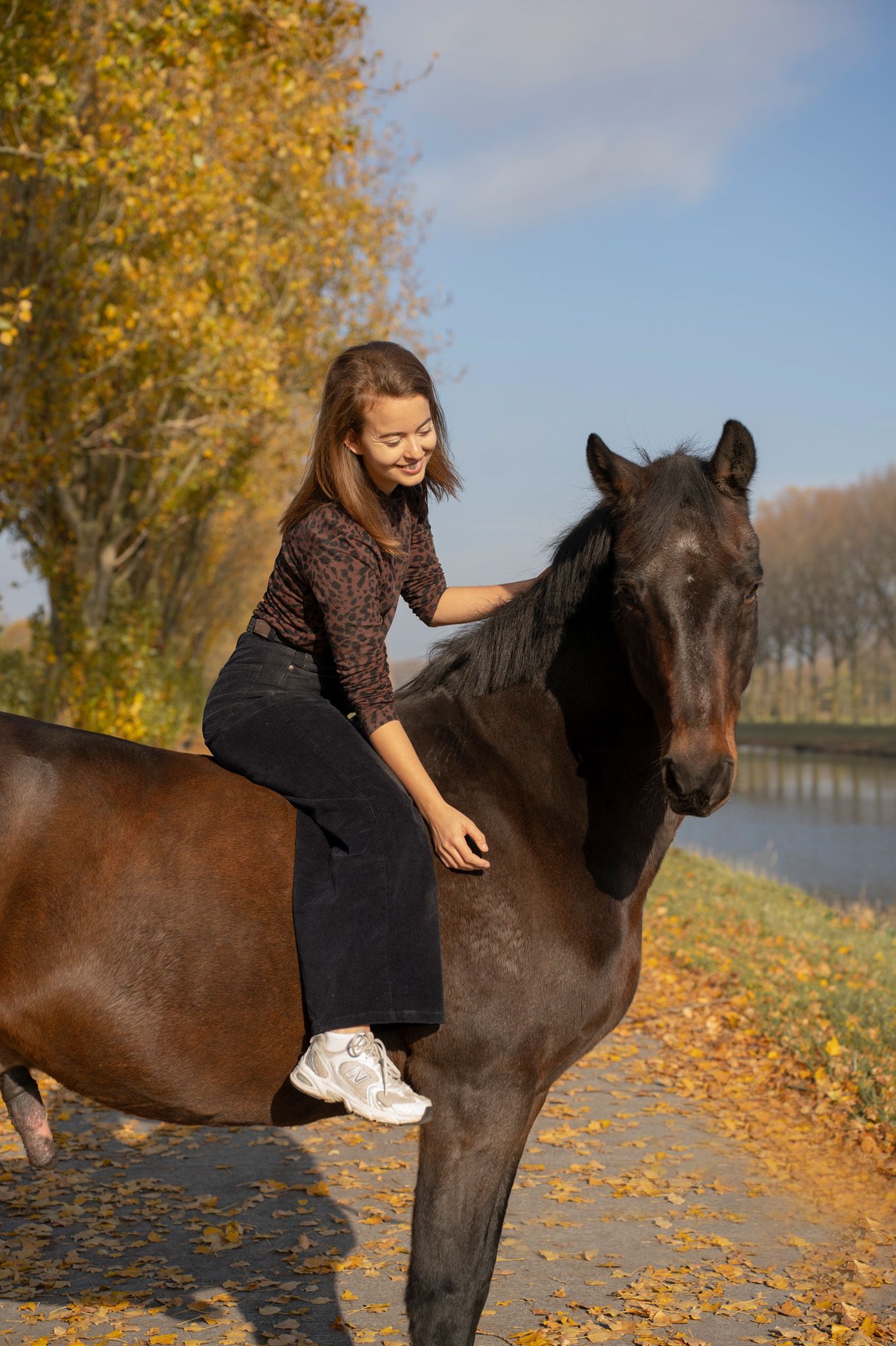 Rider sitting bareback on a dark horse during autumn by a canal.