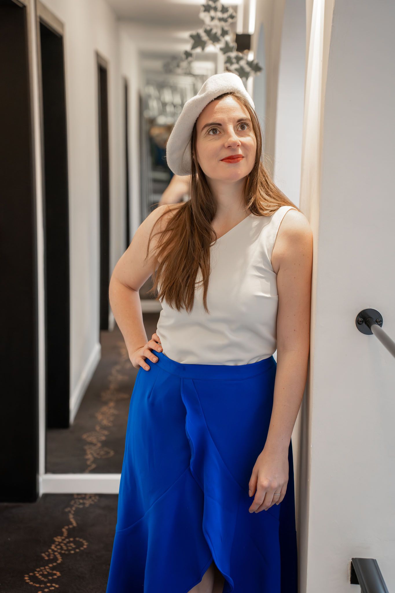 Person wearing white top and bright blue pants standing in a modern hallway.