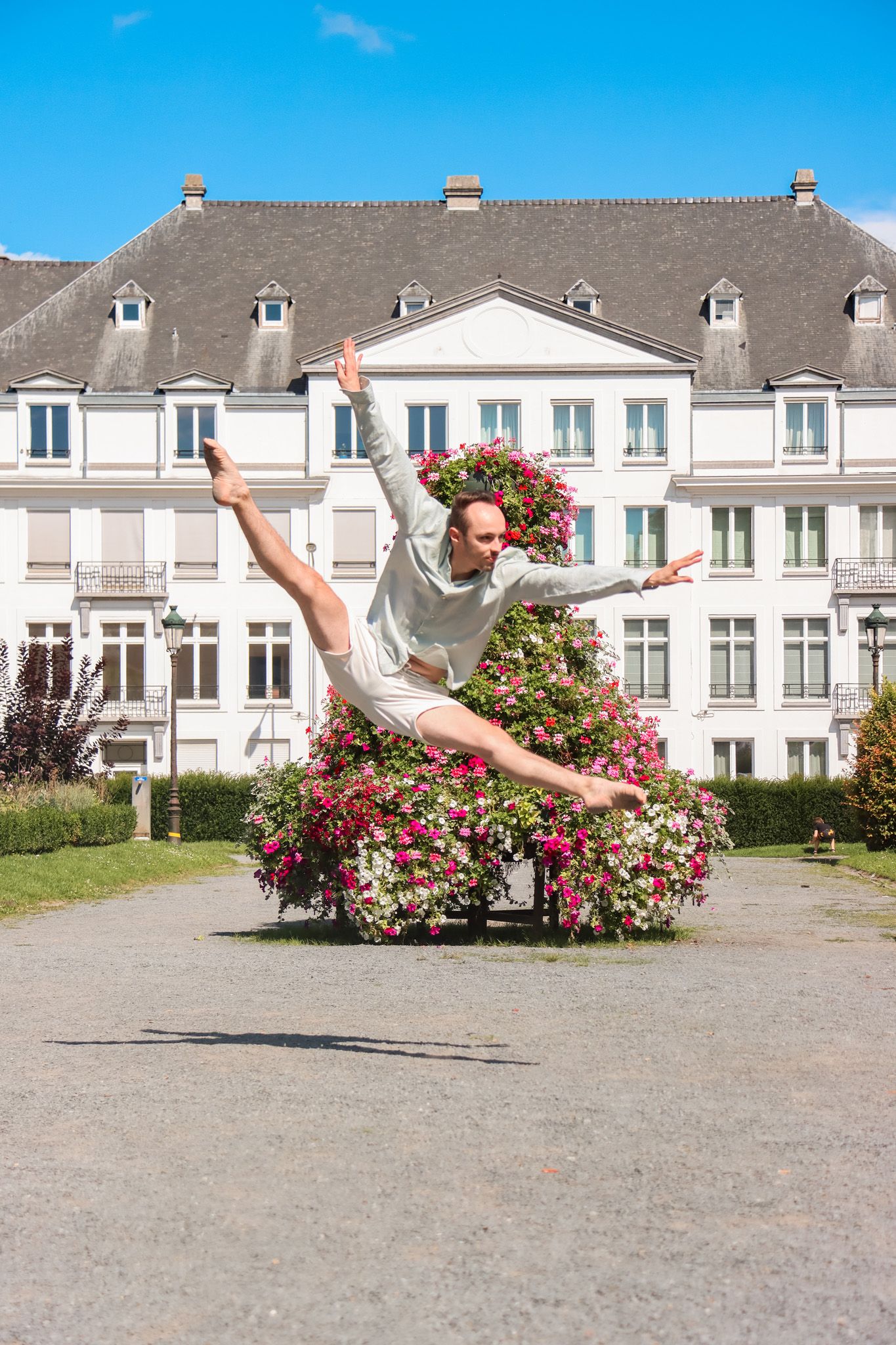 Dancer leaping through the air in front of white buildings and blooming pink flowers.