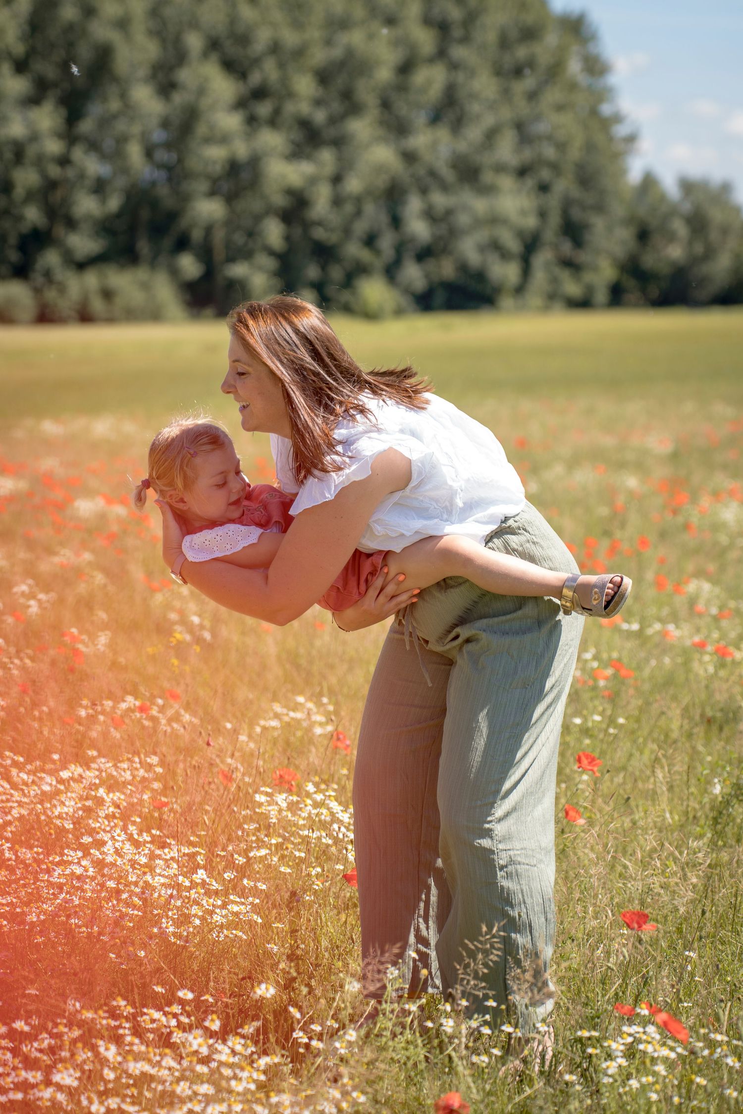 Playful outdoor photography session in a field of white daisies and red poppies.