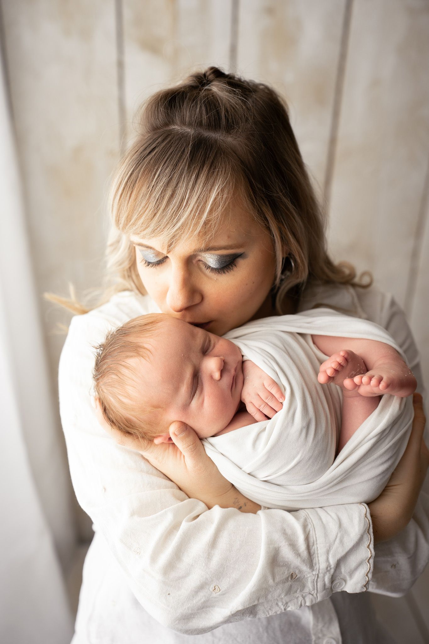 Tender moment between parent and swaddled newborn baby against light background.