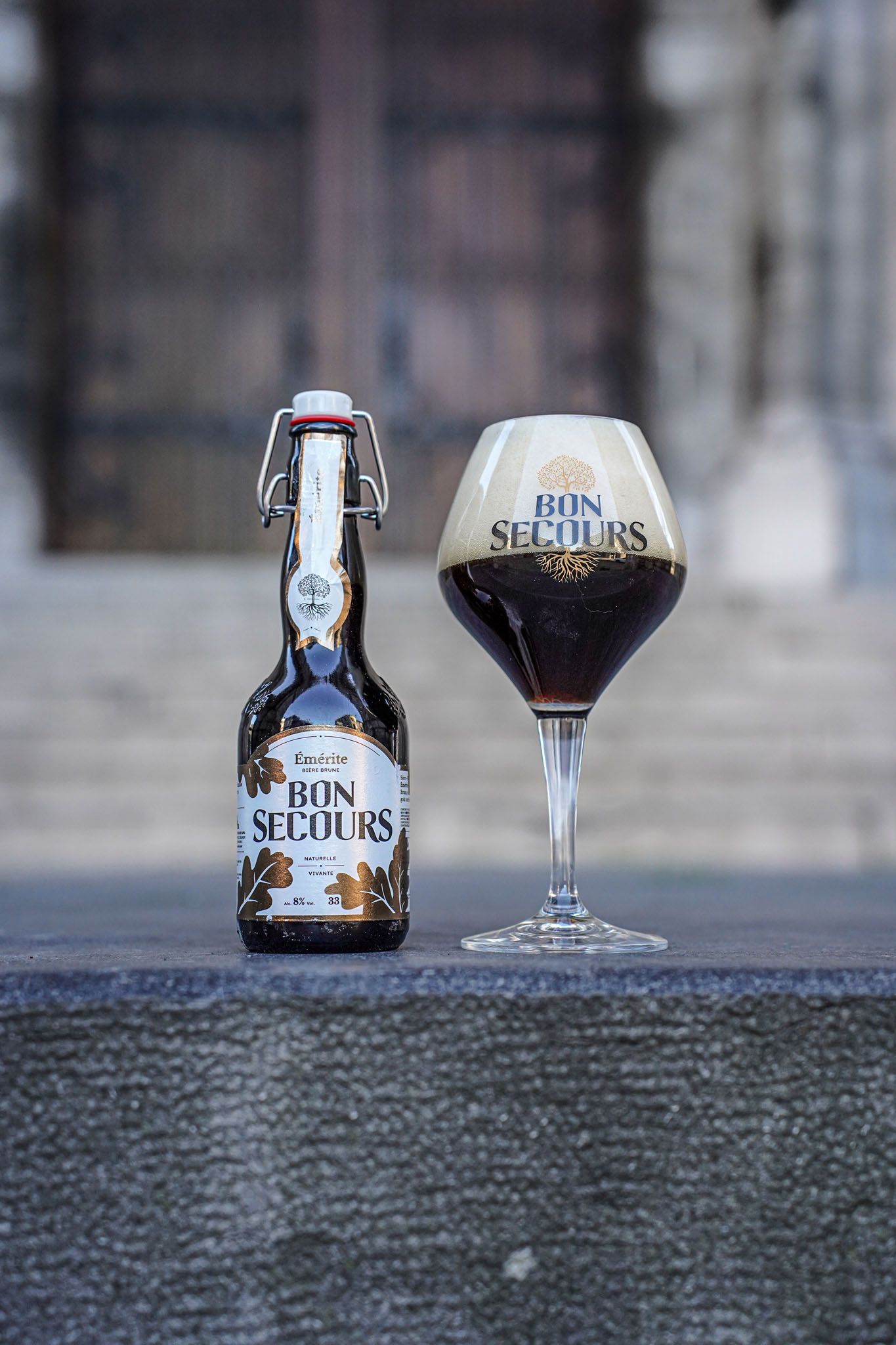 Bon Secours beer bottle and filled glass displayed on concrete surface.