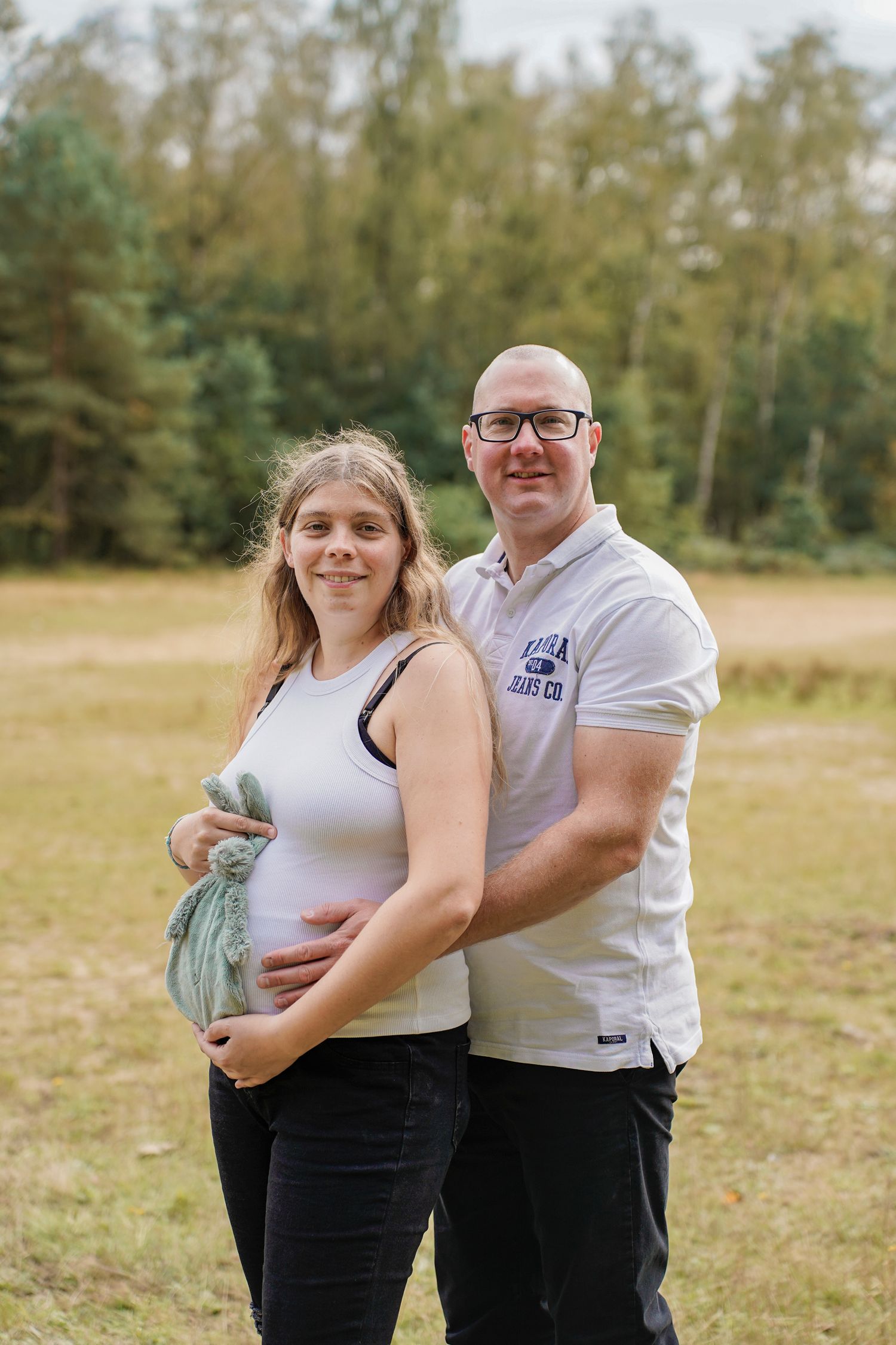 A couple poses together in a grassy field during an outdoor maternity photoshoot.