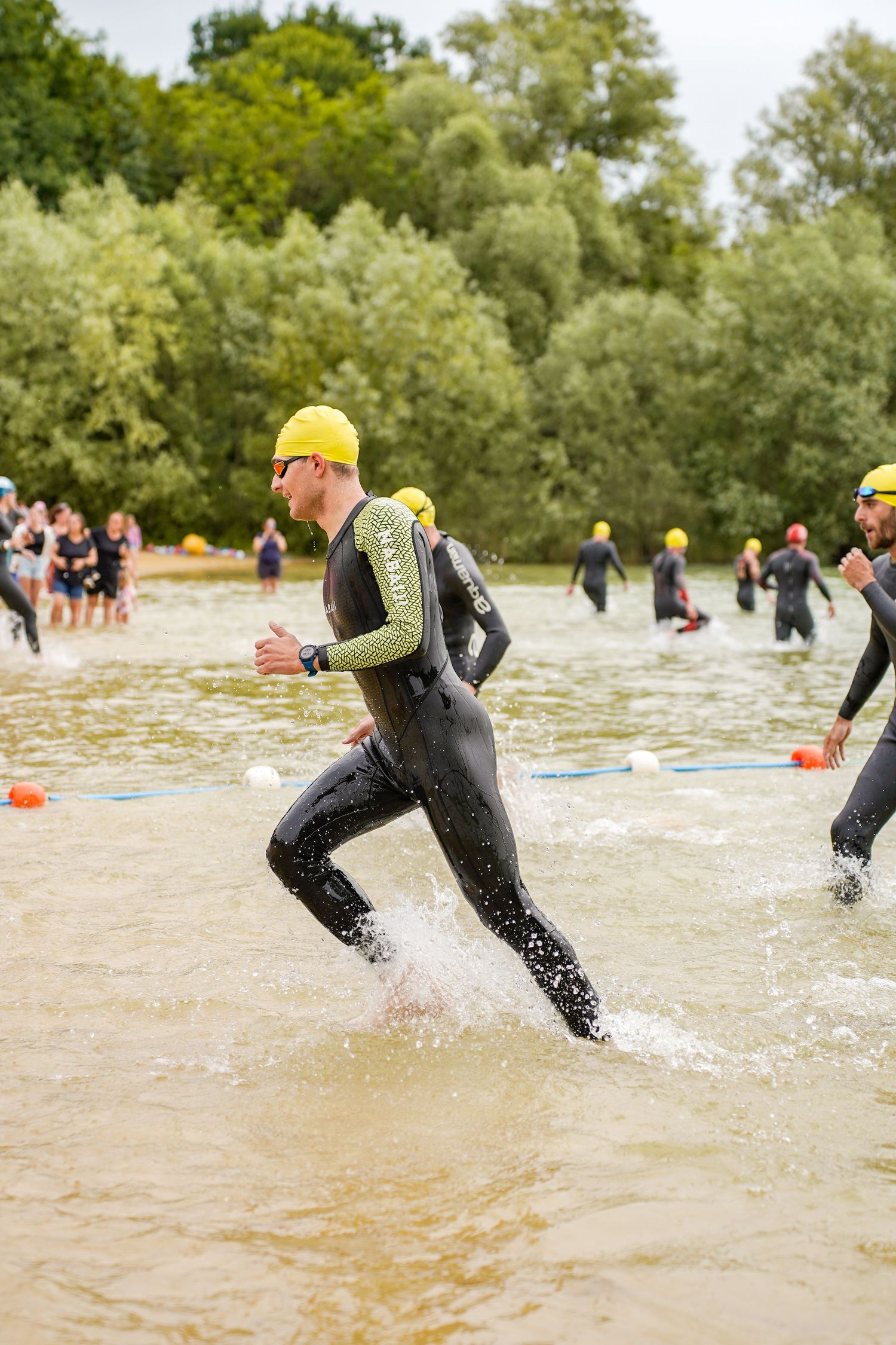 Triathletes in black wetsuits running through shallow water during race.