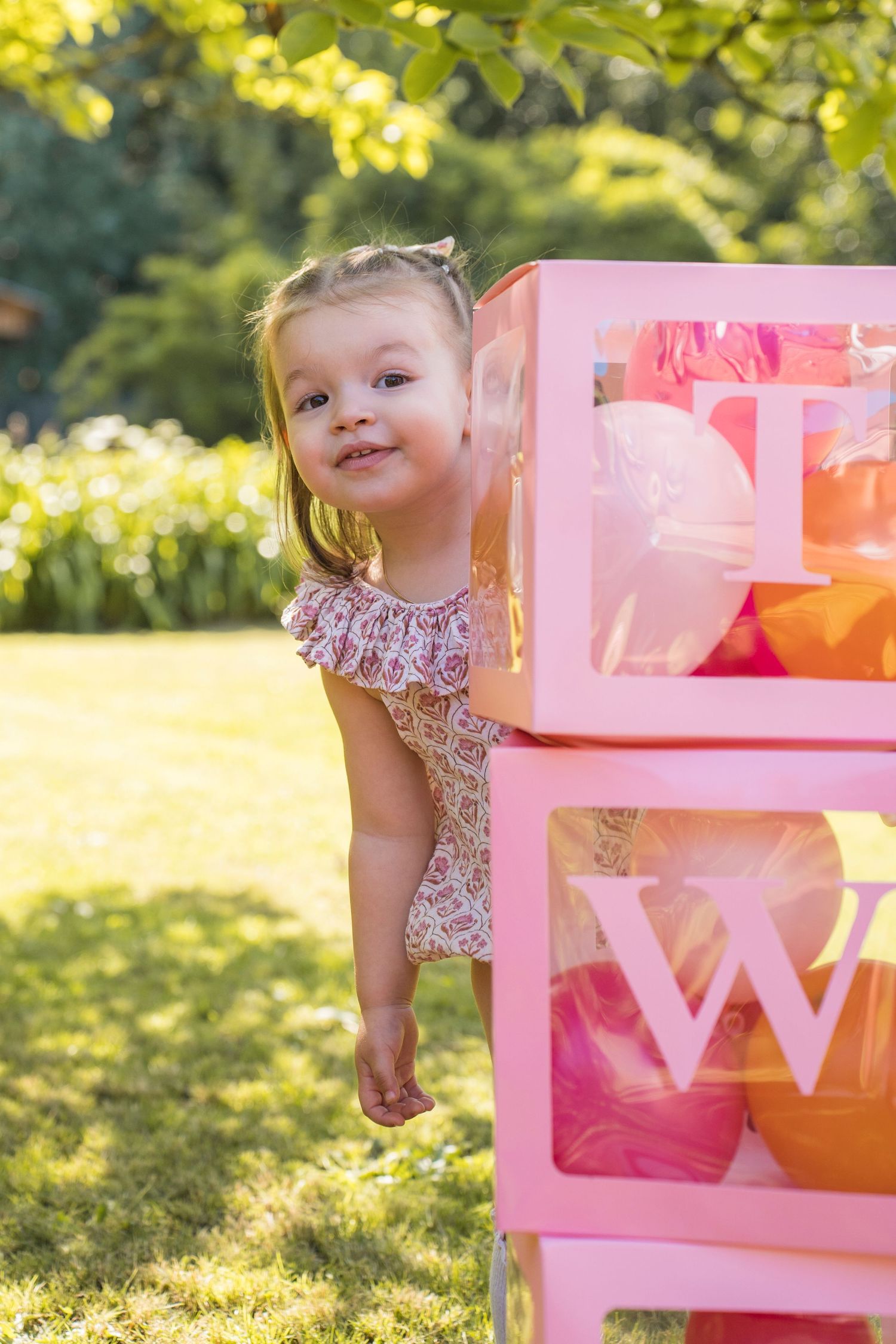 Playful scene with pink decorative boxes and floral dress against sunny outdoor background.