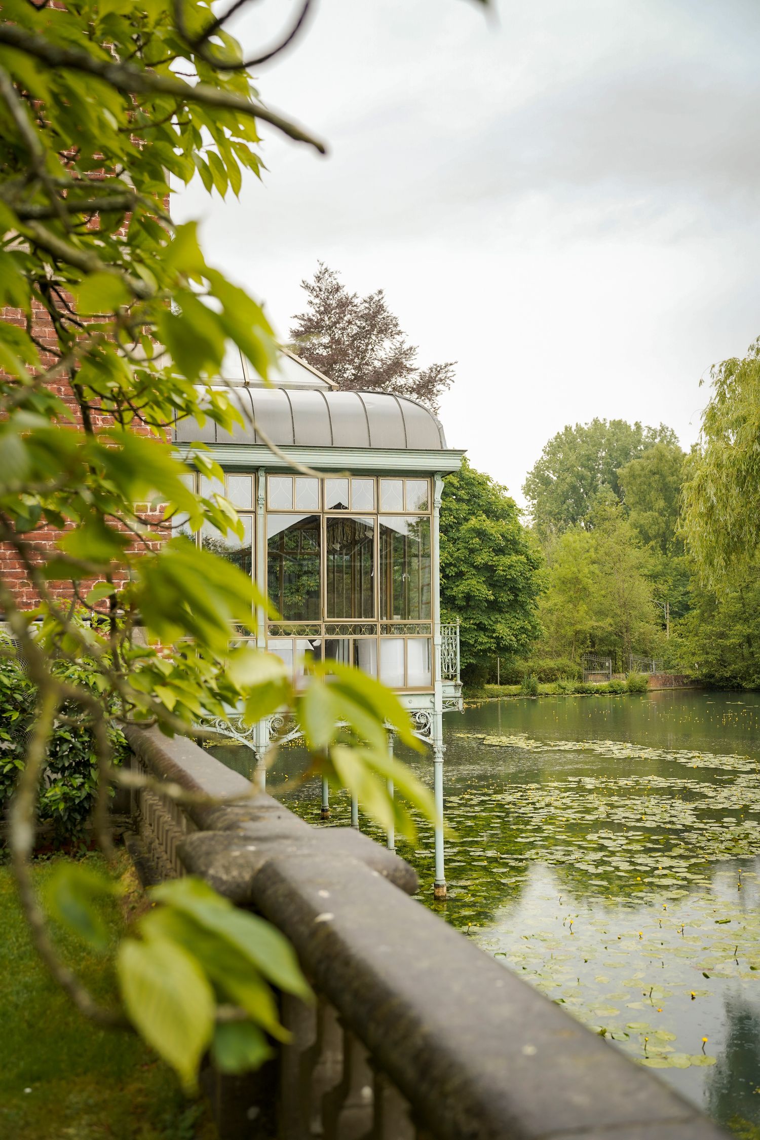 Serene pond with lily pads and white gazebo surrounded by lush green gardens.